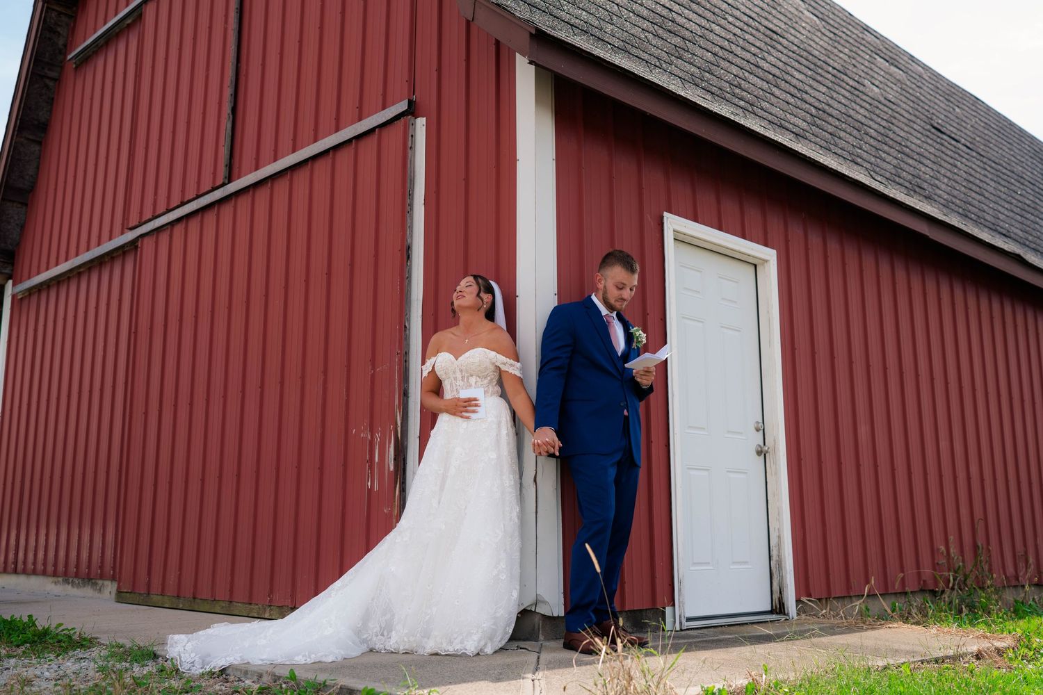 Bride and groom sharing a private moment reading vows on opposite sides of red barn door.