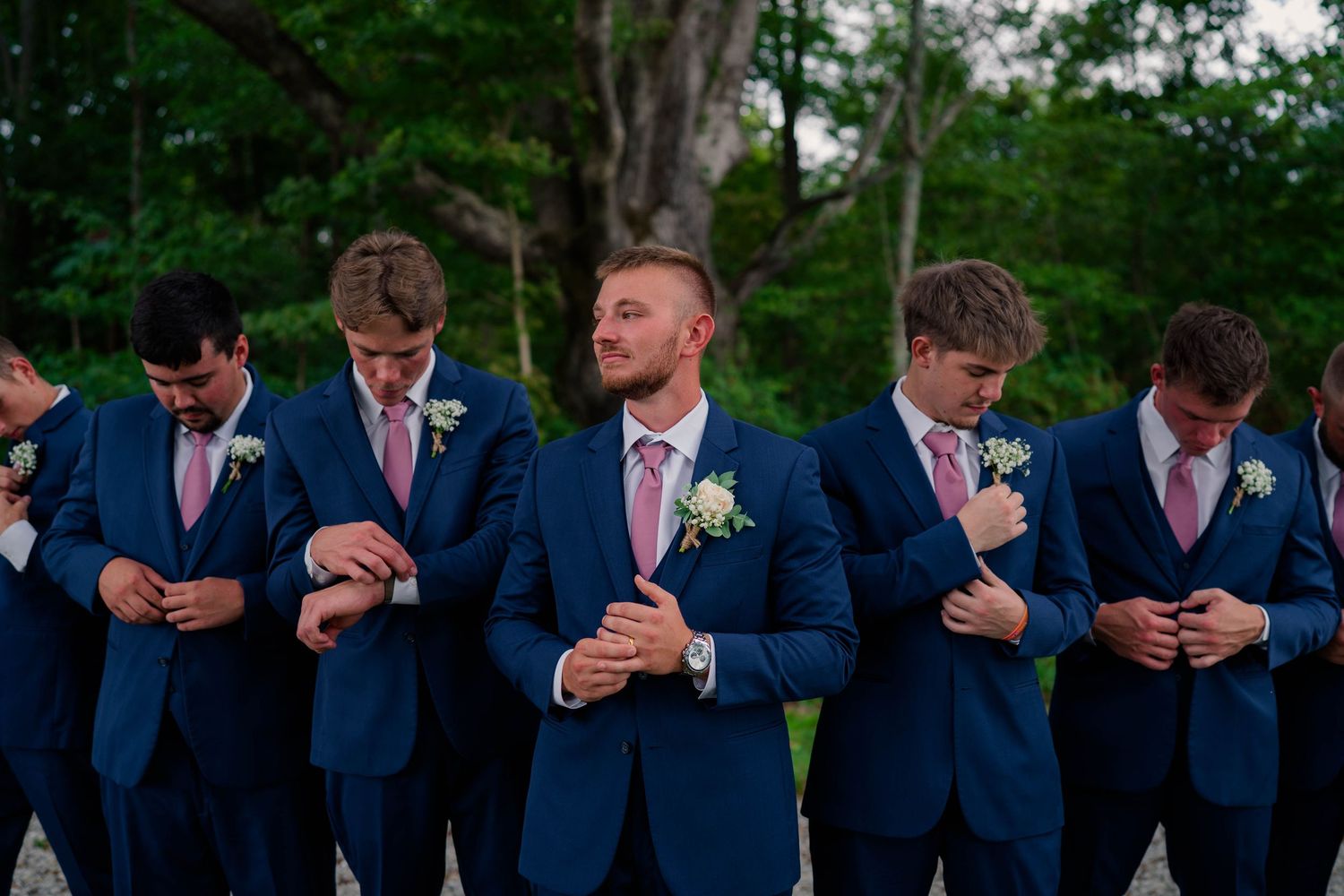Groomsmen in navy suits adjusting their cufflinks before a wedding ceremony outdoors.