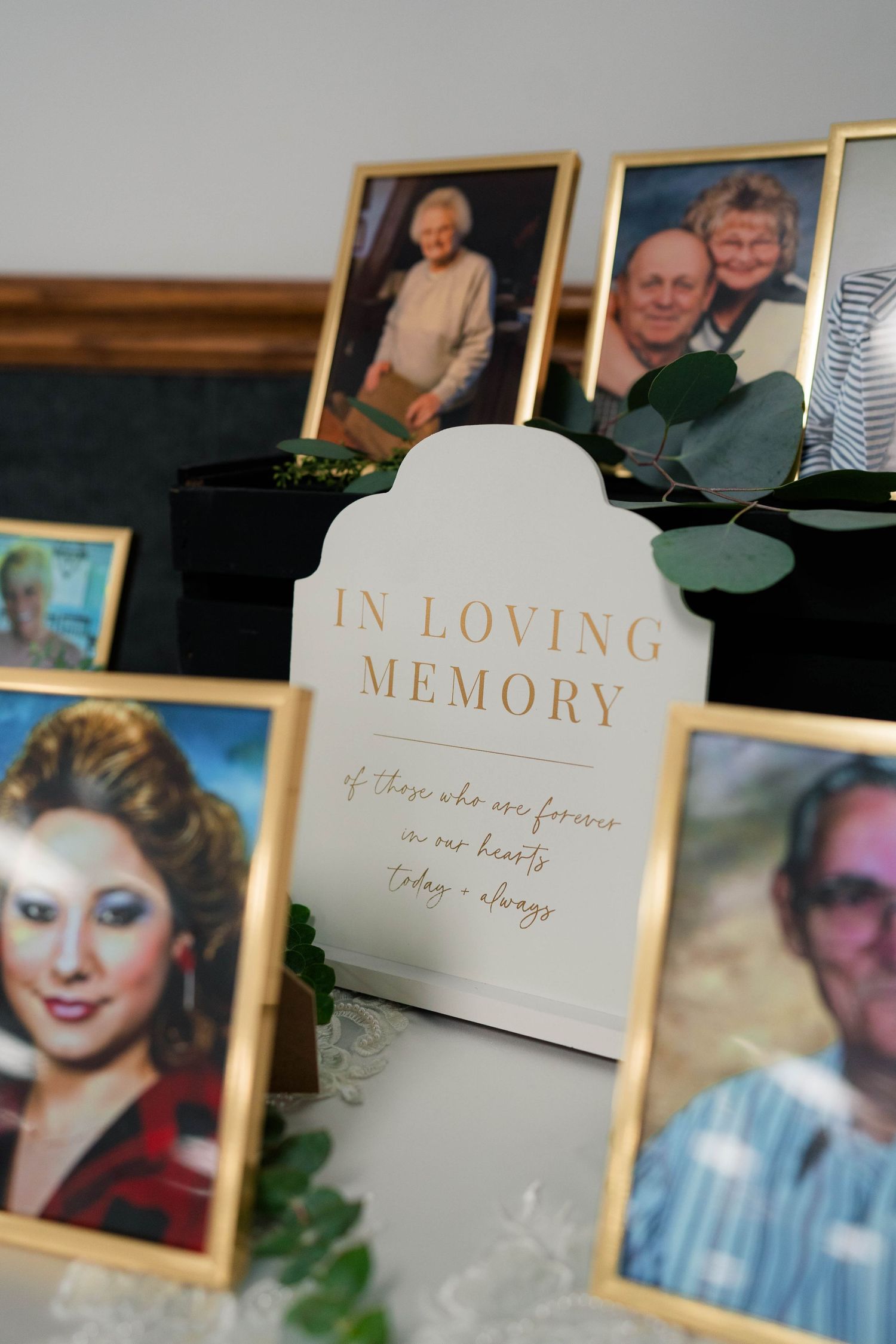 In Loving Memory wedding display with framed photos of deceased loved ones in gold frames.