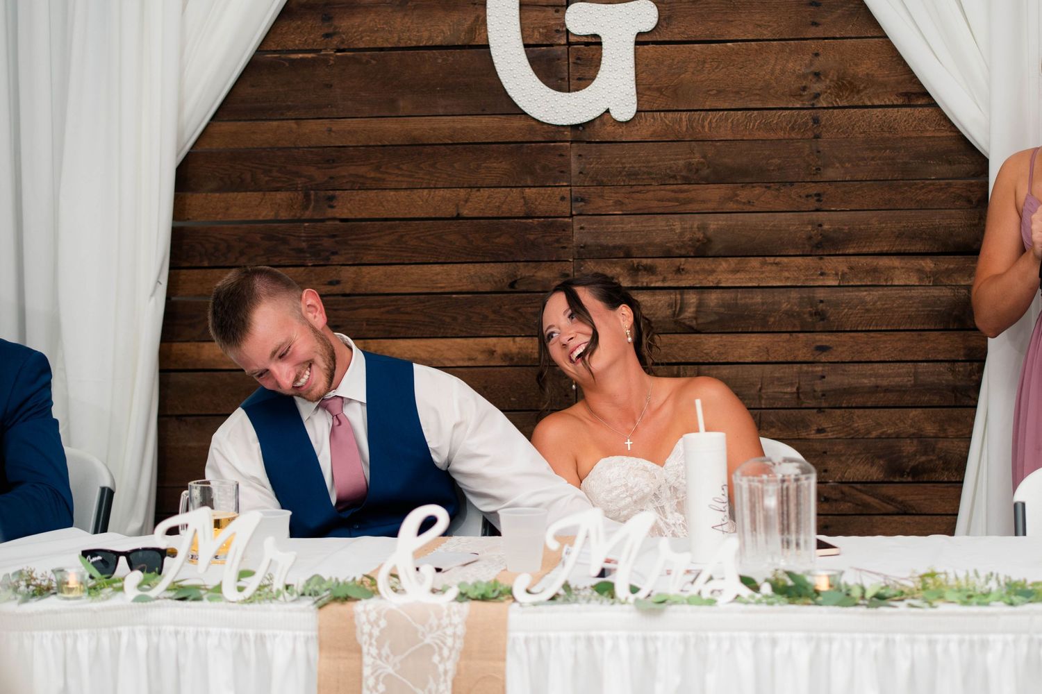 Bride and groom share a joyful laugh together at sweetheart table during wedding reception.