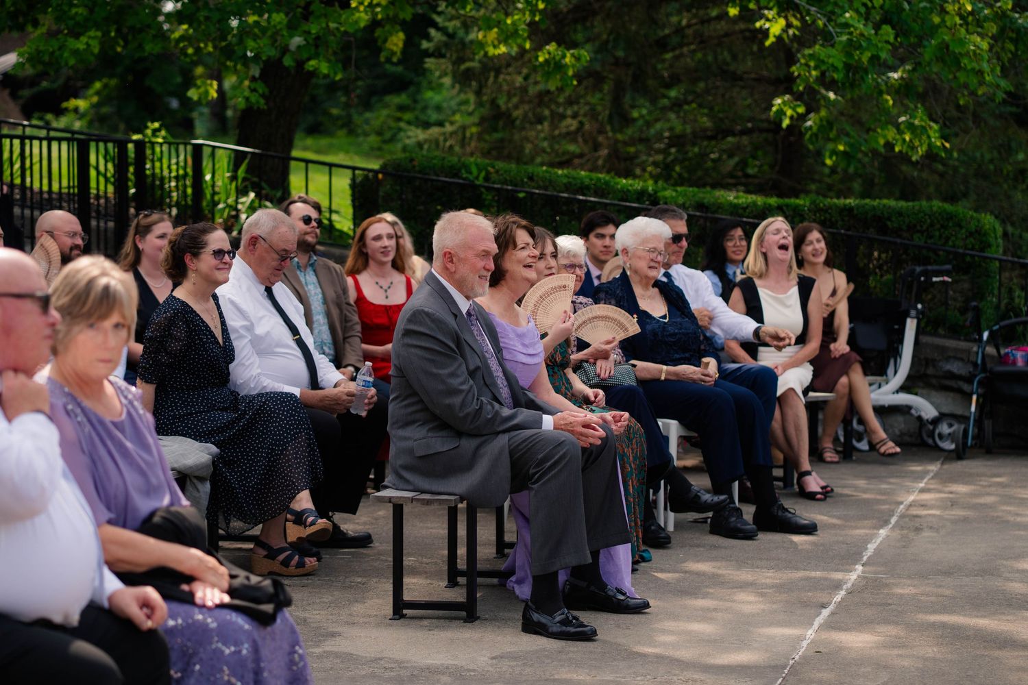 Wedding guests seated outdoors in sunlight watching a garden wedding ceremony.