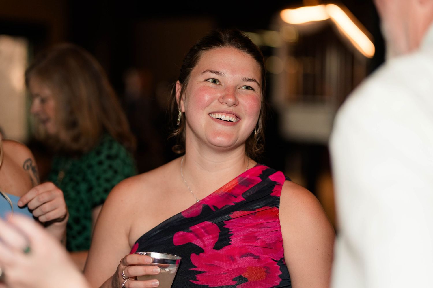Smiling woman in colorful floral dress holding a drink at a social gathering.