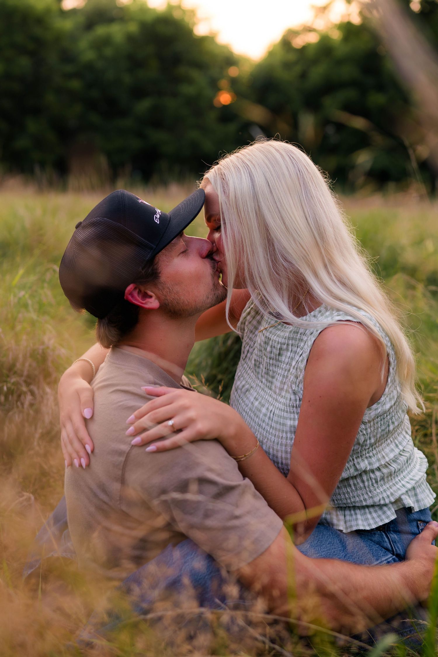 Couple sharing a romantic kiss while sitting in a golden grass field at sunset.
