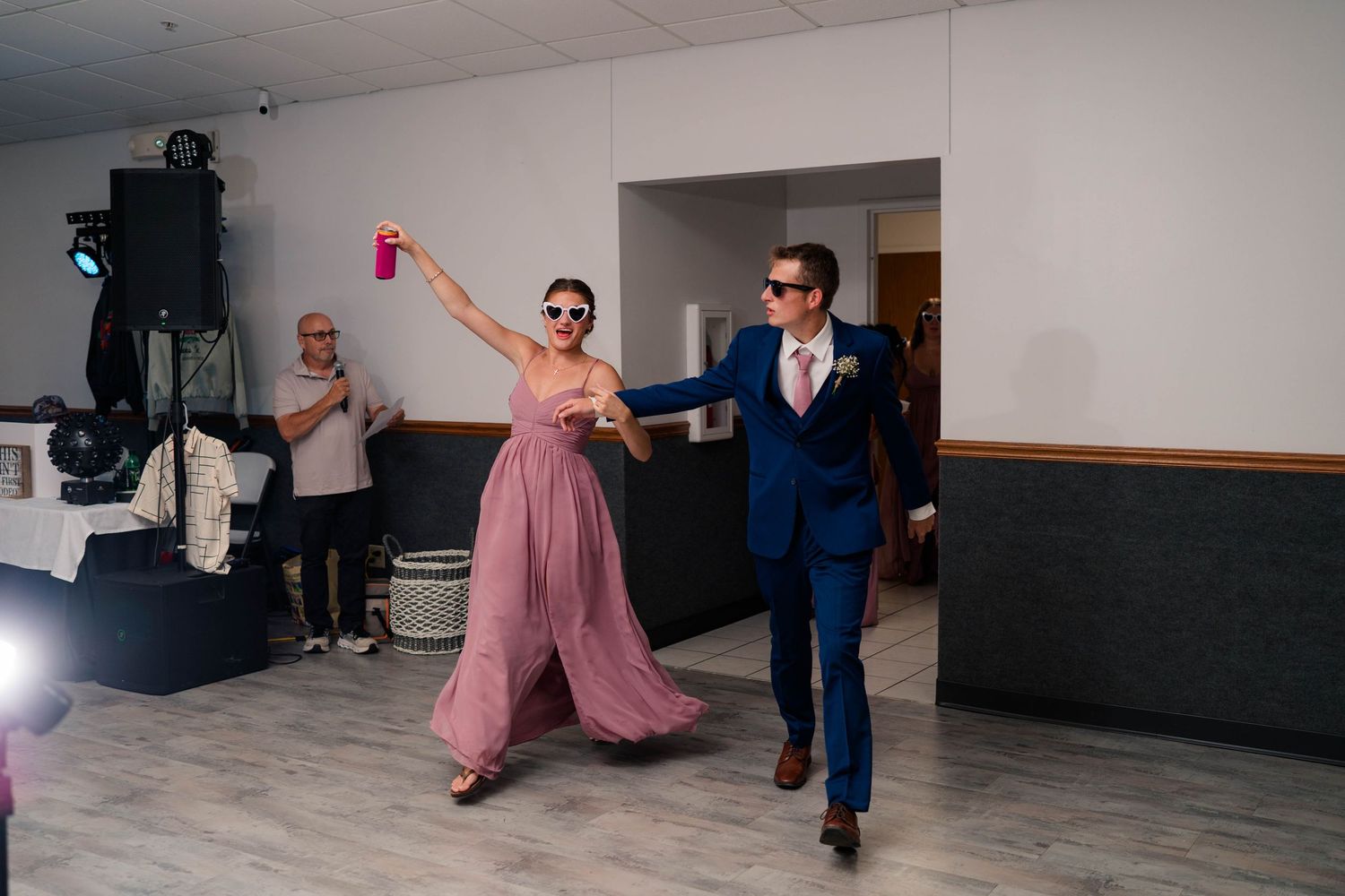 Bridesmaid in pink gown and groomsman in navy suit make grand entrance at reception.