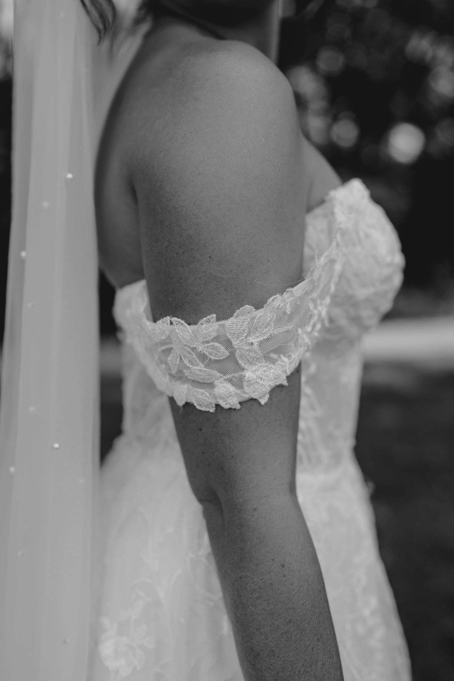 Black and white close-up detail of bride's off-shoulder lace wedding gown sleeve and veil.