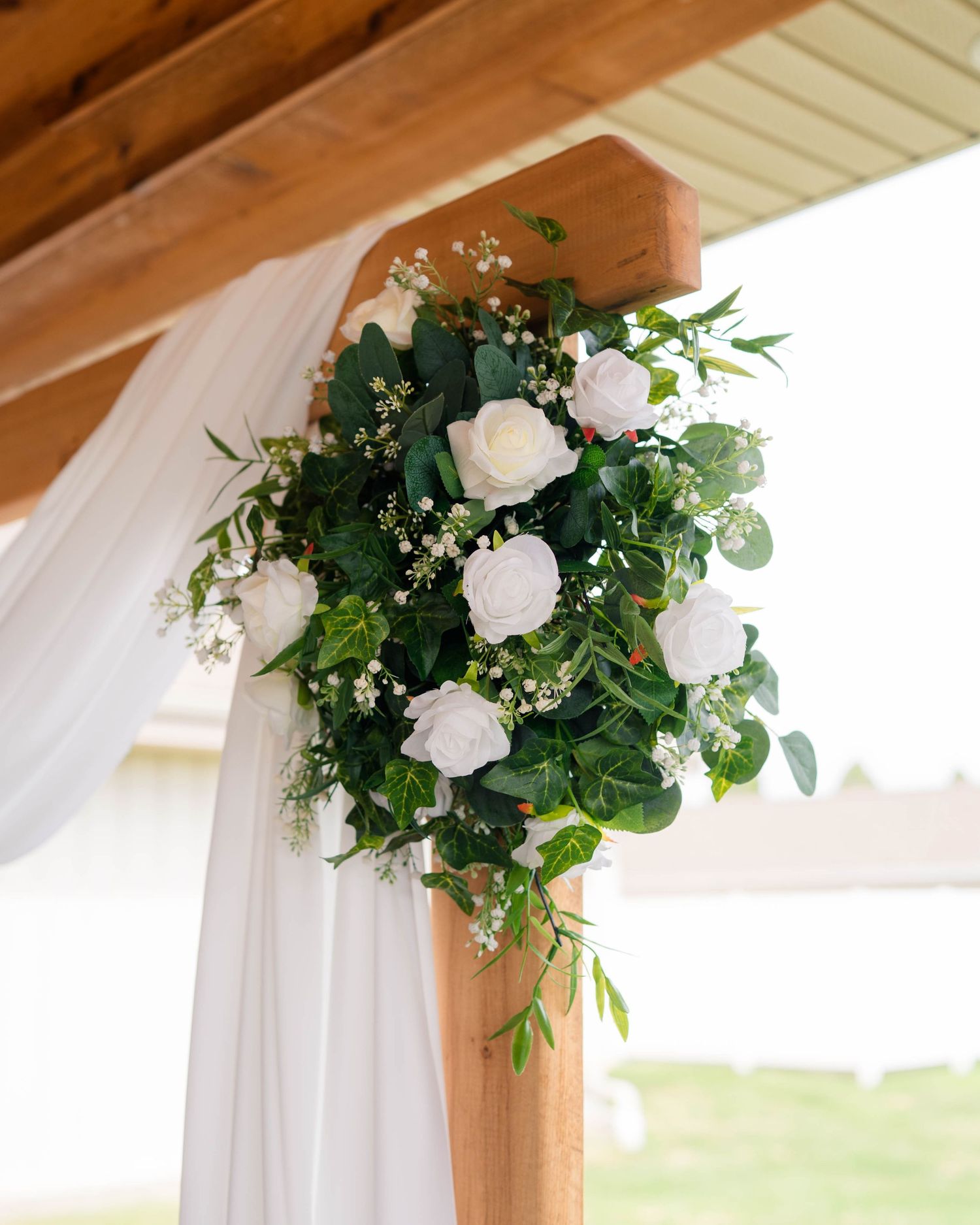 Elegant wedding arch decorated with white roses, eucalyptus, and baby's breath with flowing white draping.