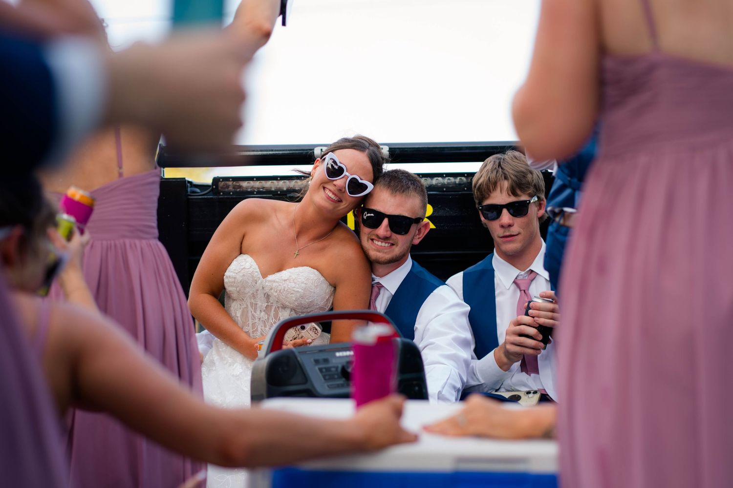 Bride and groom wear novelty sunglasses posing together at outdoor wedding reception with guests nearby.