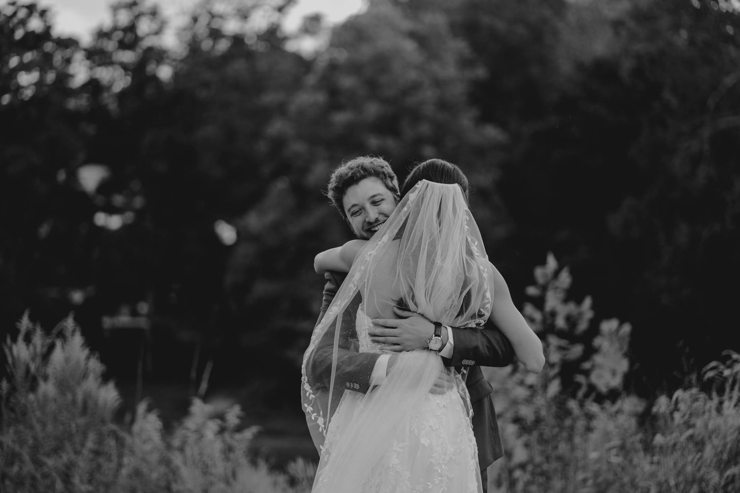 A groom embraces his bride in a black and white outdoor wedding photo.