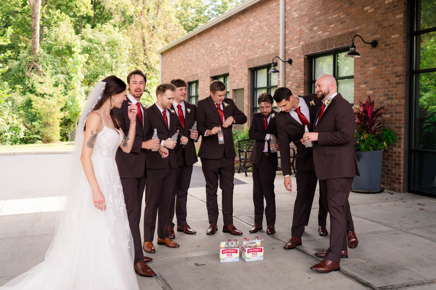 Bride and groom celebrate with groomsmen in dark suits outside rustic brick wedding venue.