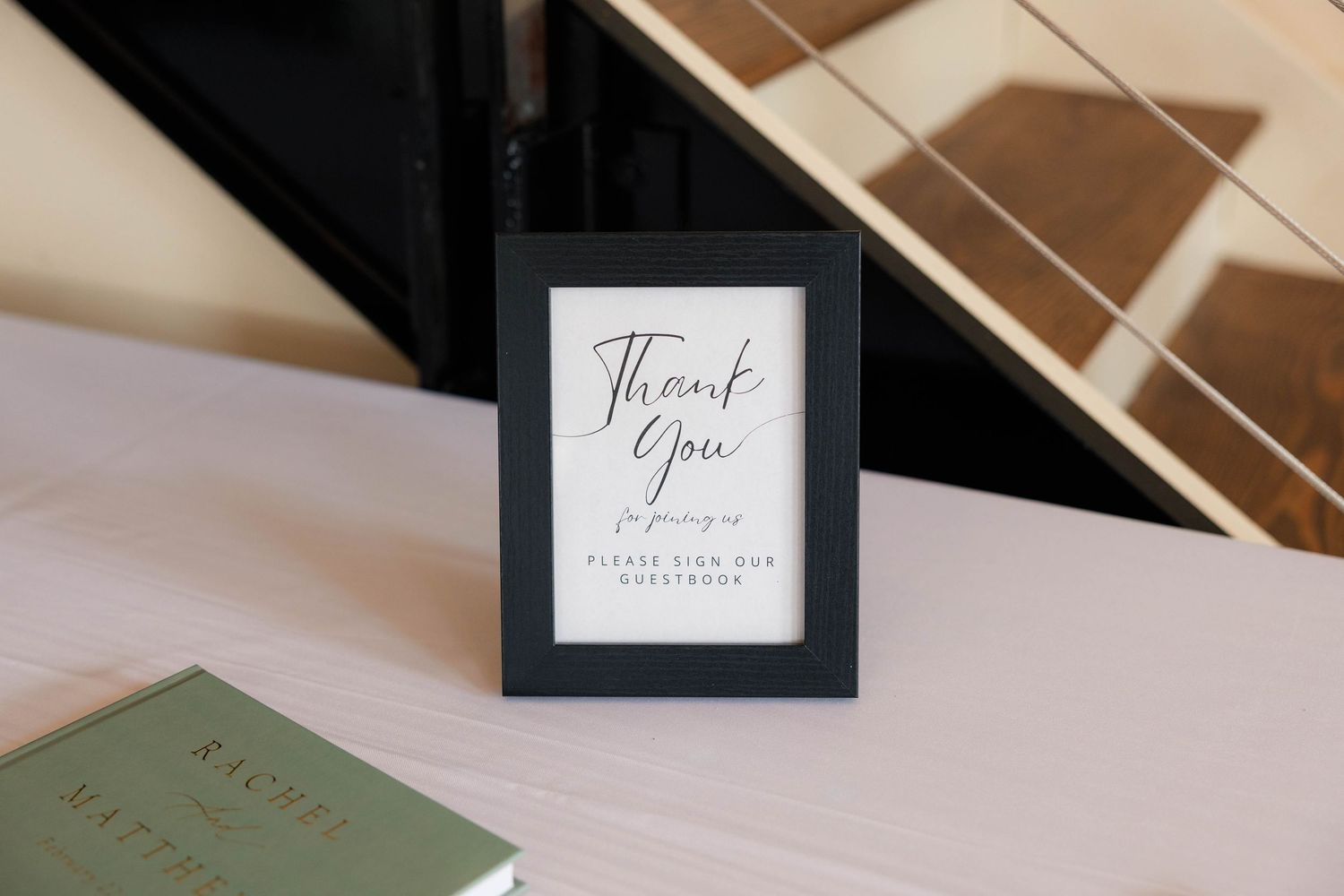 Black framed thank you sign asking guests to sign the guestbook, displayed next to a Rachel book at a wedding.