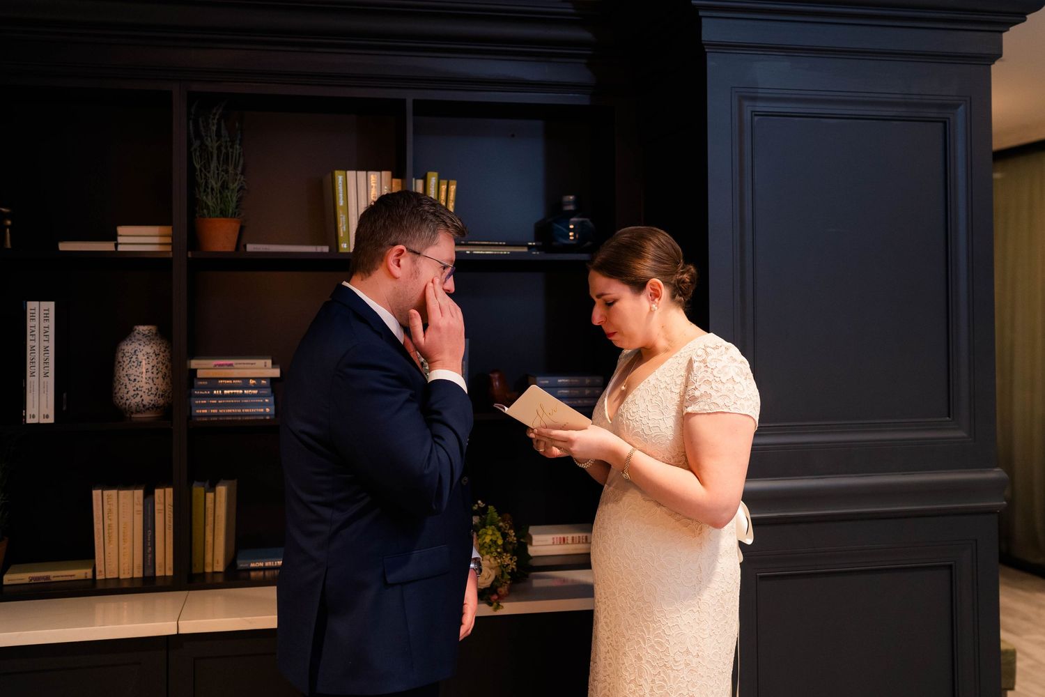 Groom overcome with emotion covering mouth as bride reads heartfelt wedding vows from paper.