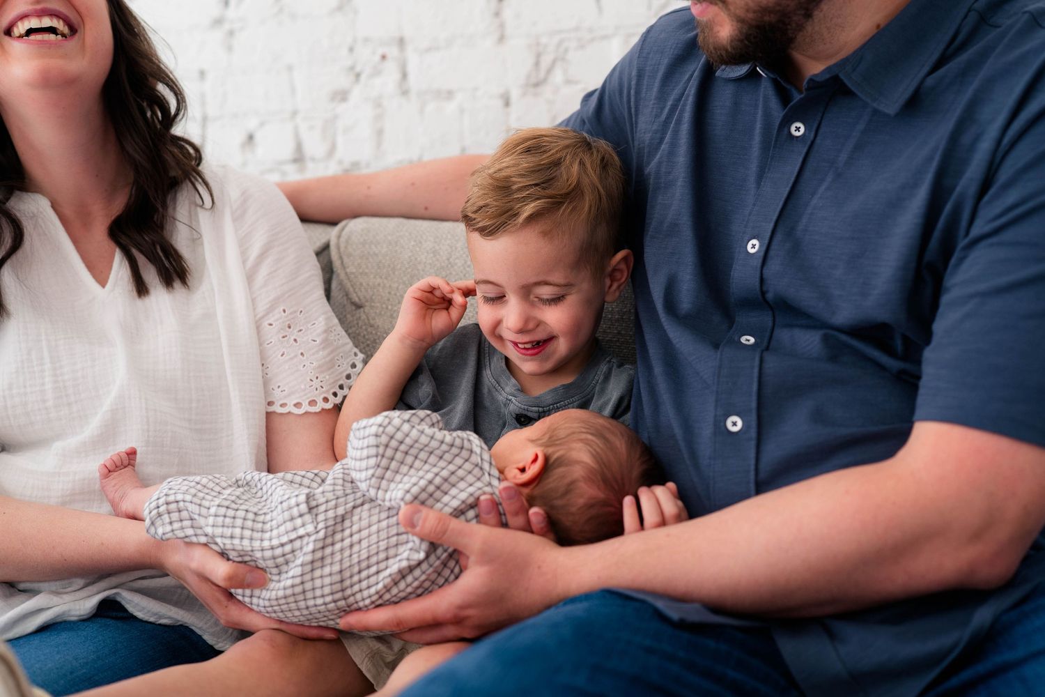 Happy family with parents and toddler admiring their newborn baby wrapped in a gray blanket while sitting together.