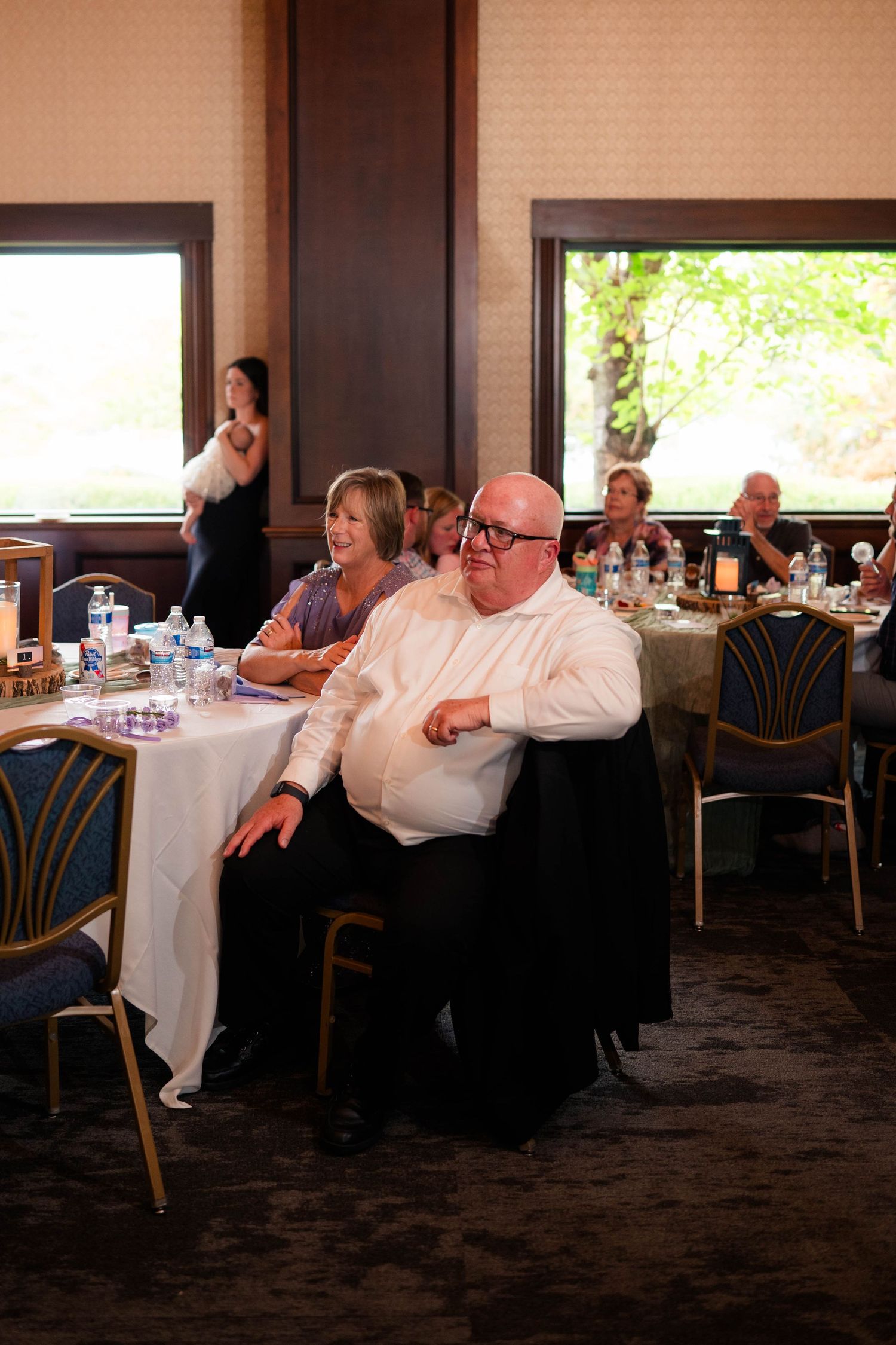 Wedding reception guests seated at round tables, smiling and enjoying the celebration in a warmly lit banquet hall.