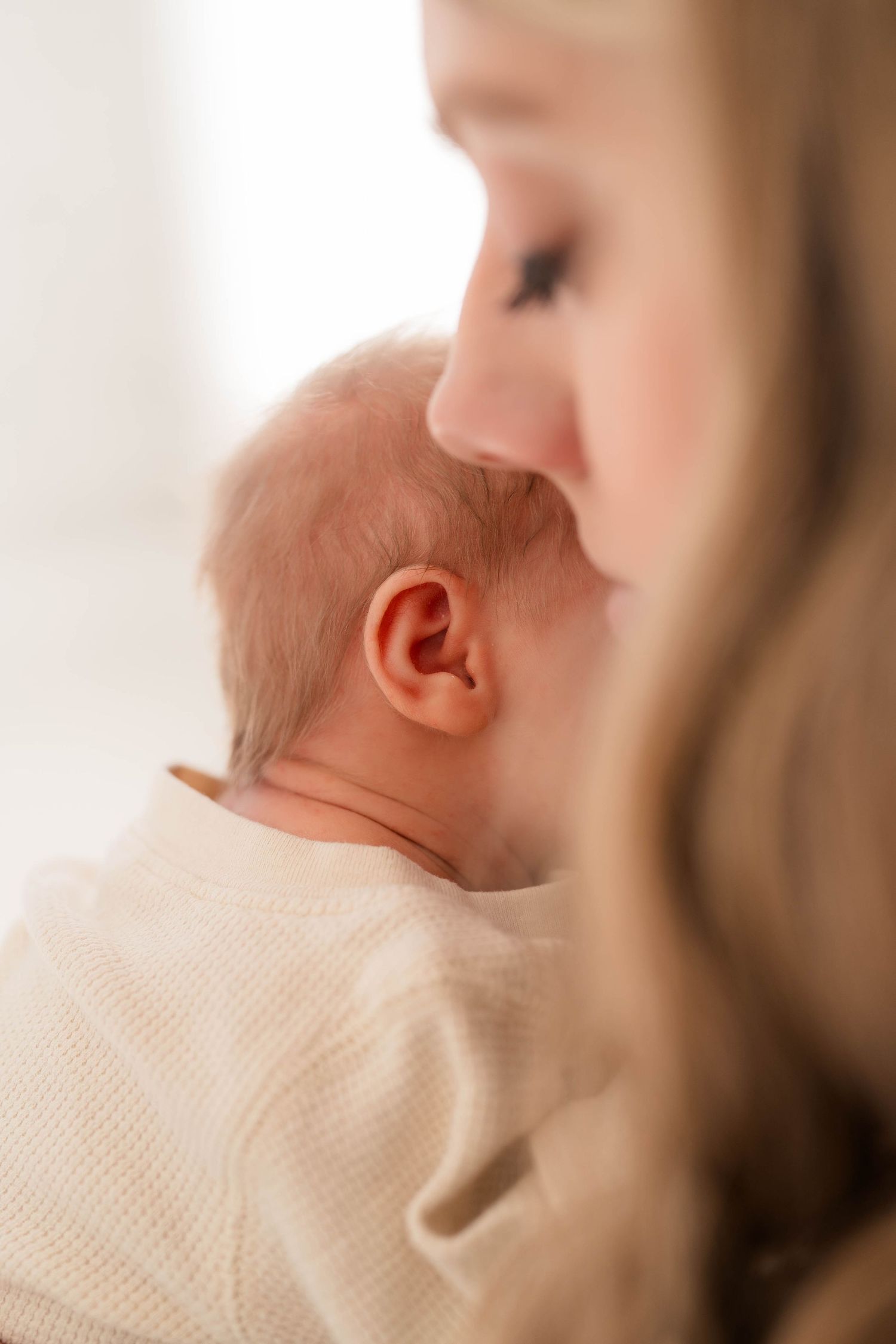 Tender close-up of a mother kissing her newborn baby on the head, captured in soft natural light.