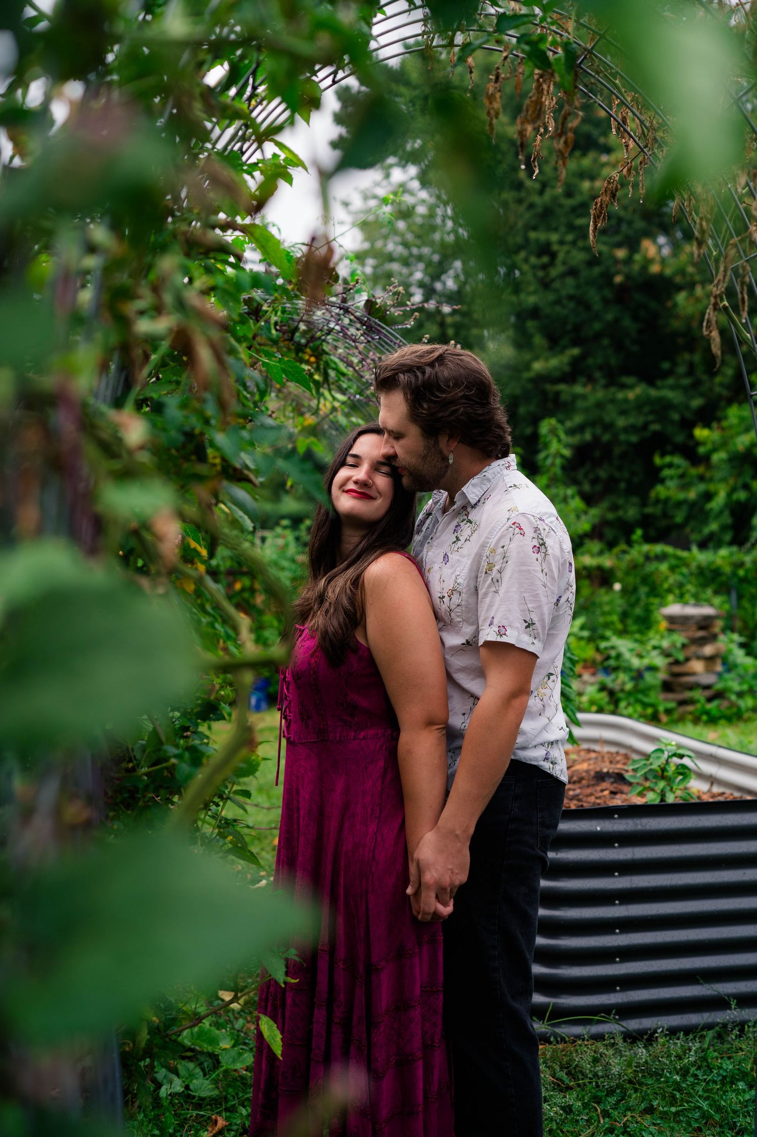 Man kissing woman on cheek as she smiles in a vibrant garden setting.