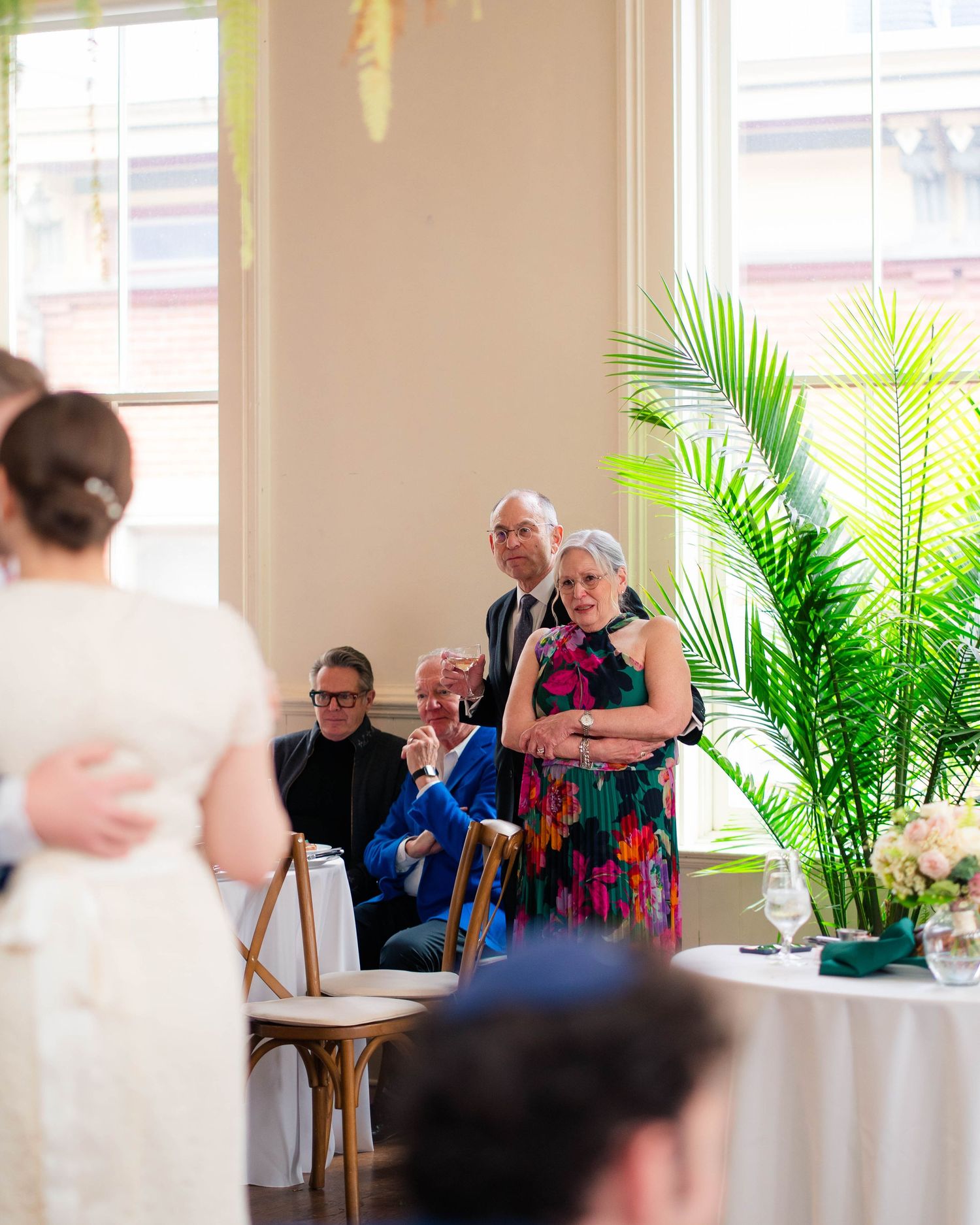 Wedding guests watching ceremony emotionally in bright botanical reception venue.