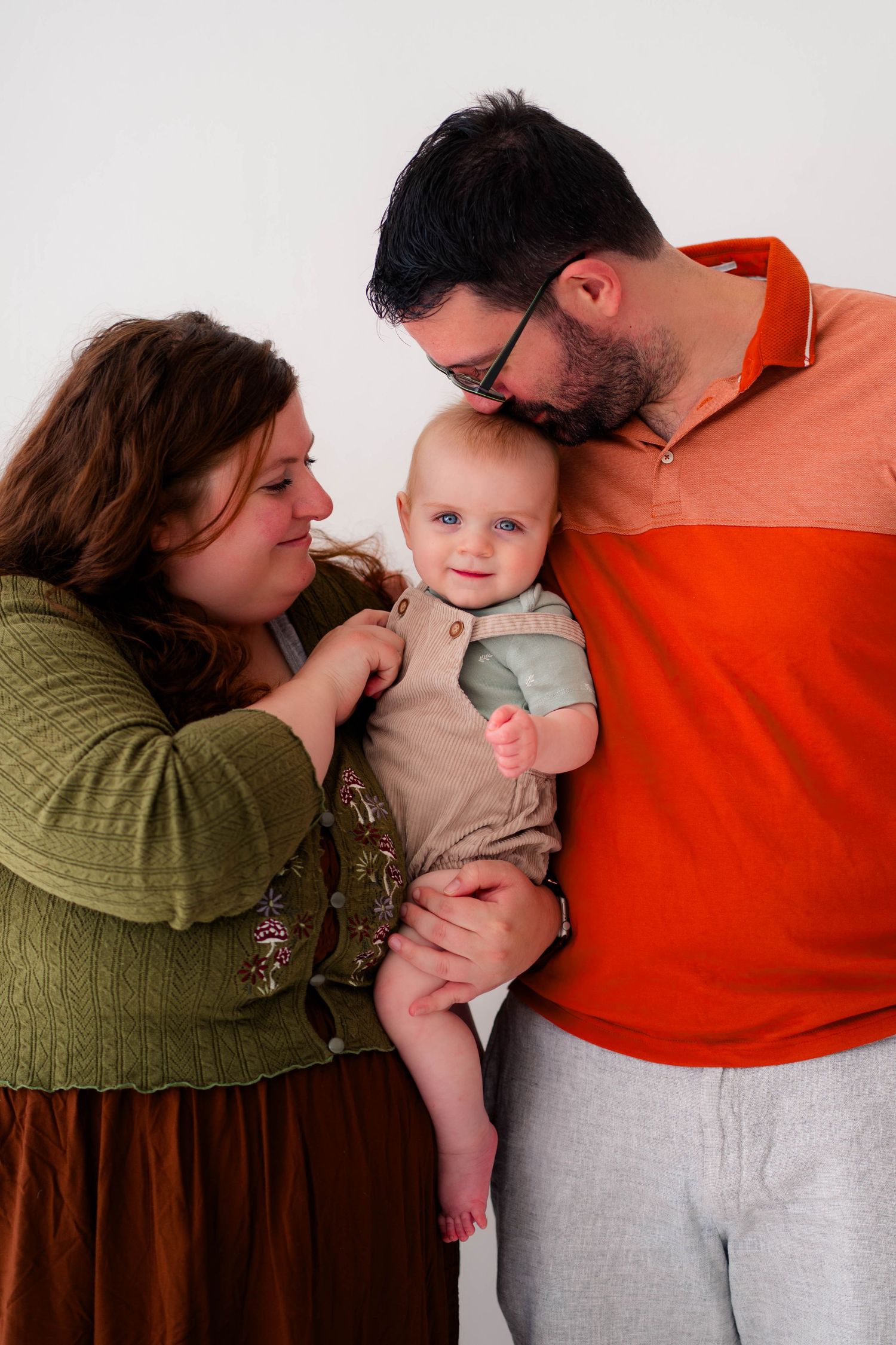 Parents lovingly holding their smiling baby in a studio portrait against white background.