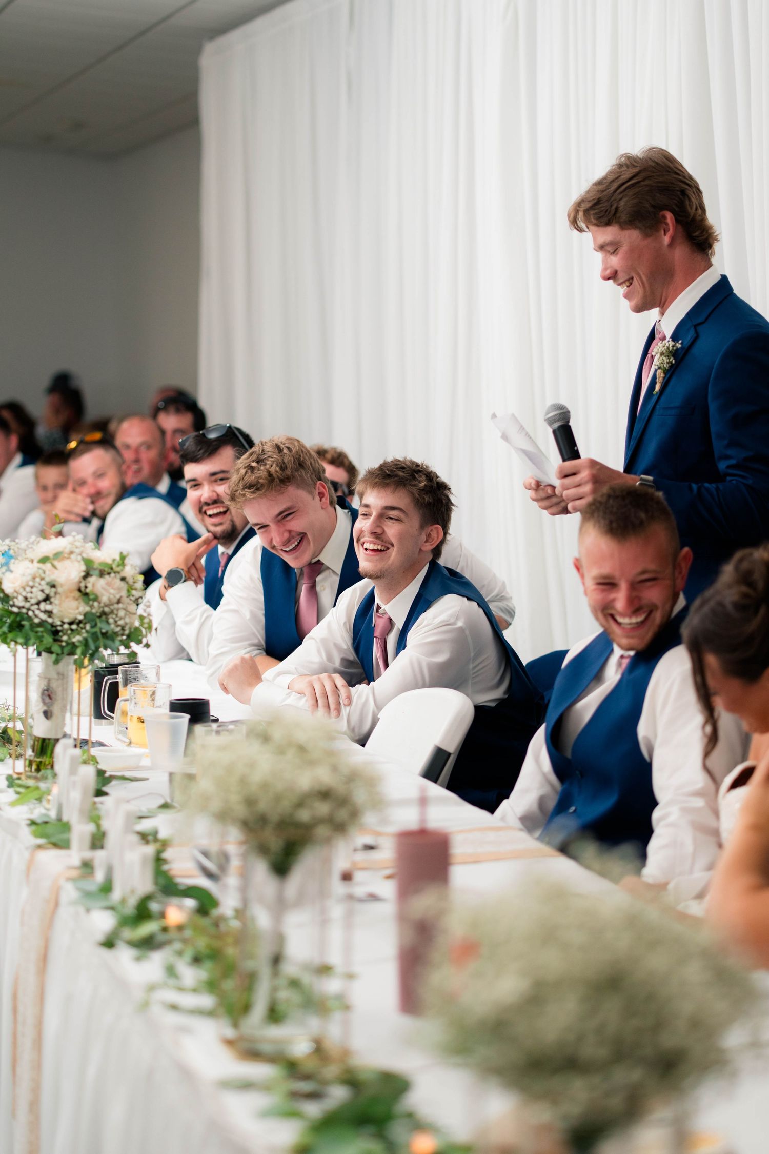 Groomsmen laughing at wedding reception head table during best man speech.