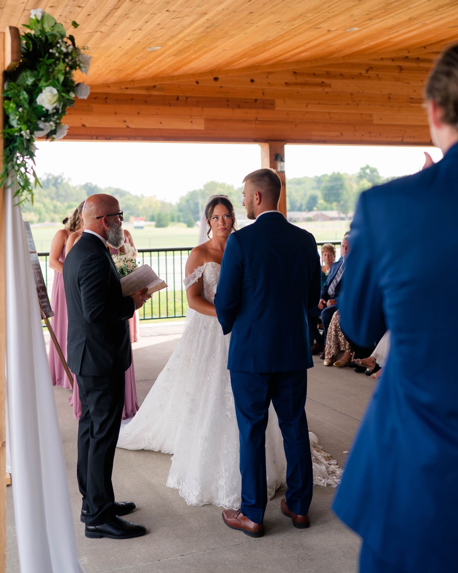 Bride and groom exchange vows at outdoor wedding ceremony under floral arch with officiant.