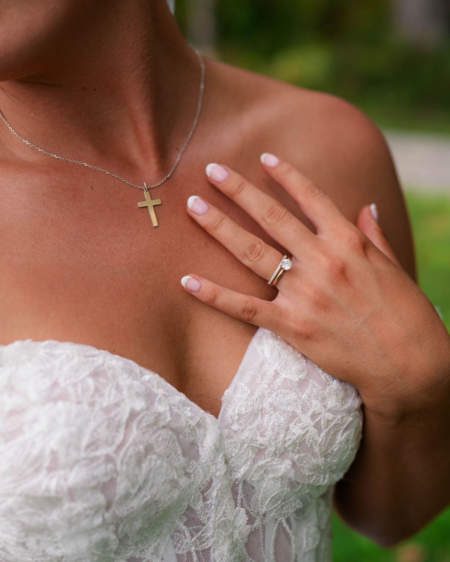 Close-up of bride wearing a gold cross necklace and wedding ring in a lace strapless bridal gown.