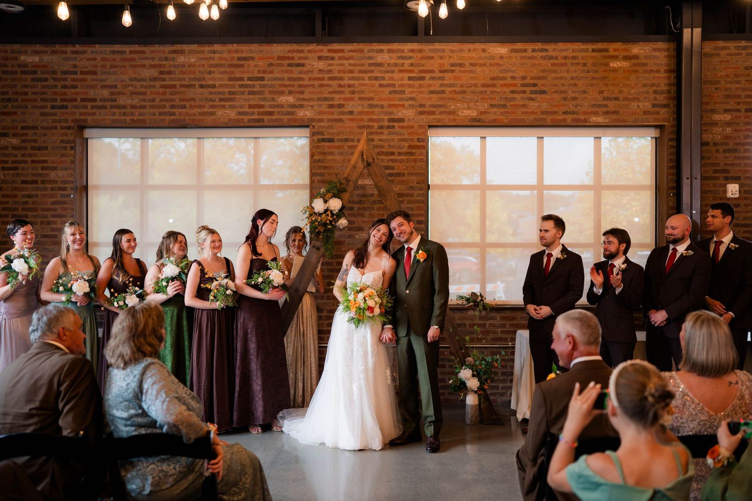 Newlyweds share a joyful moment at the altar surrounded by bridesmaids and groomsmen during wedding ceremony.