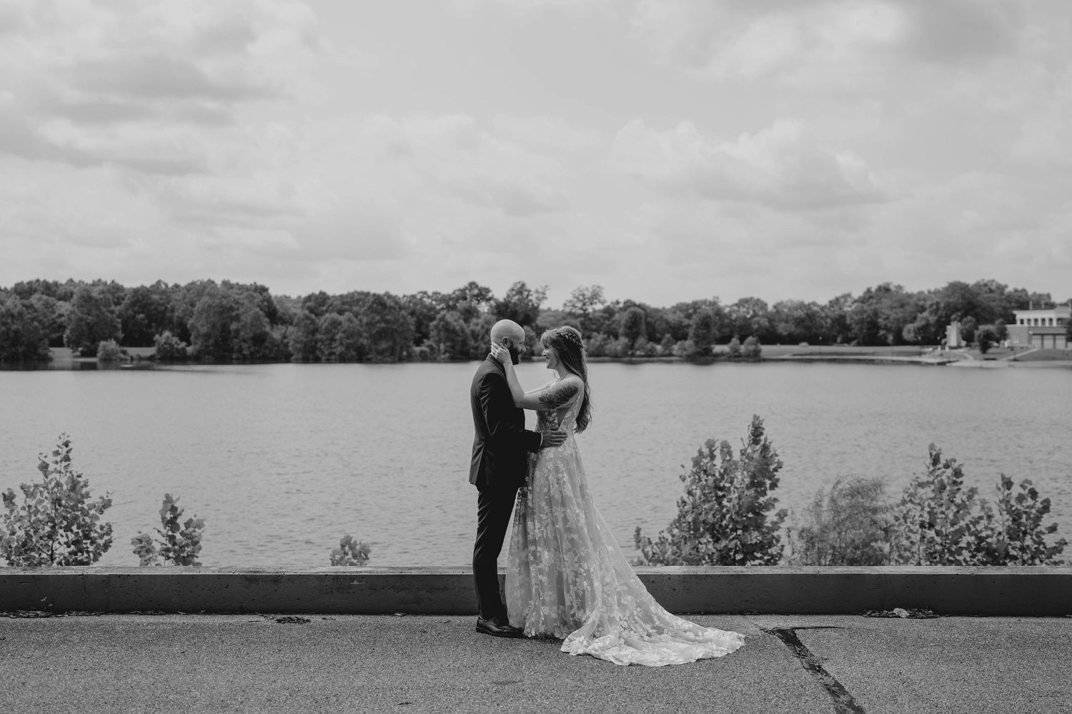 Black and white photo of bride and groom sharing romantic moment by lakeside on their wedding day.
