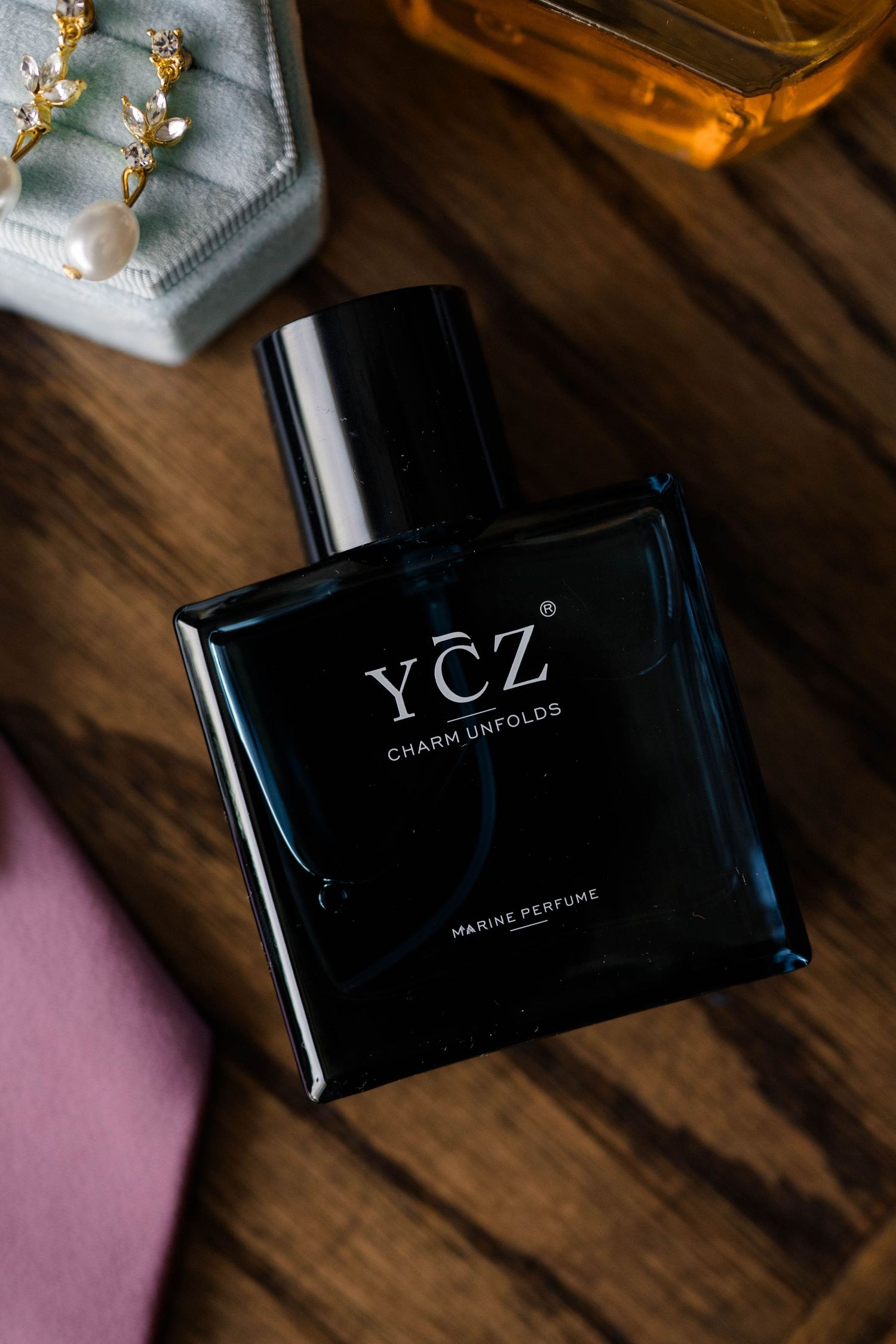 YCZ Charm Unfolds Marine Perfume black bottle on wooden surface with jewelry and accessories.