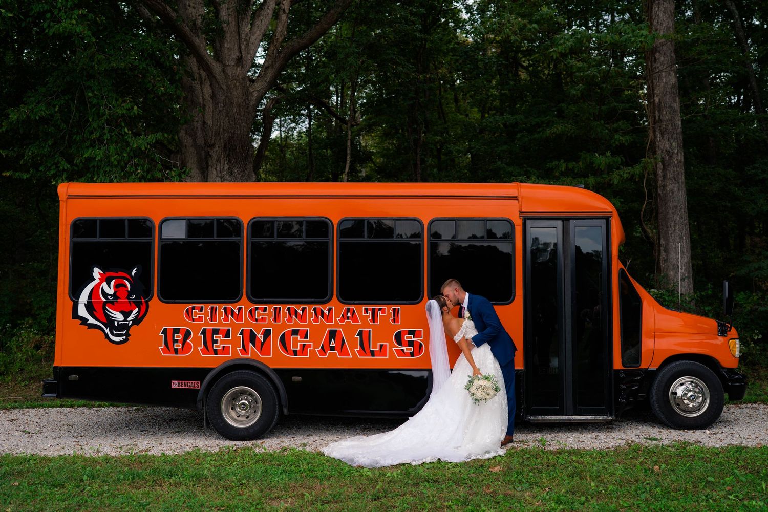 Bride and groom share a kiss in front of a Cincinnati Bengals themed orange party bus.