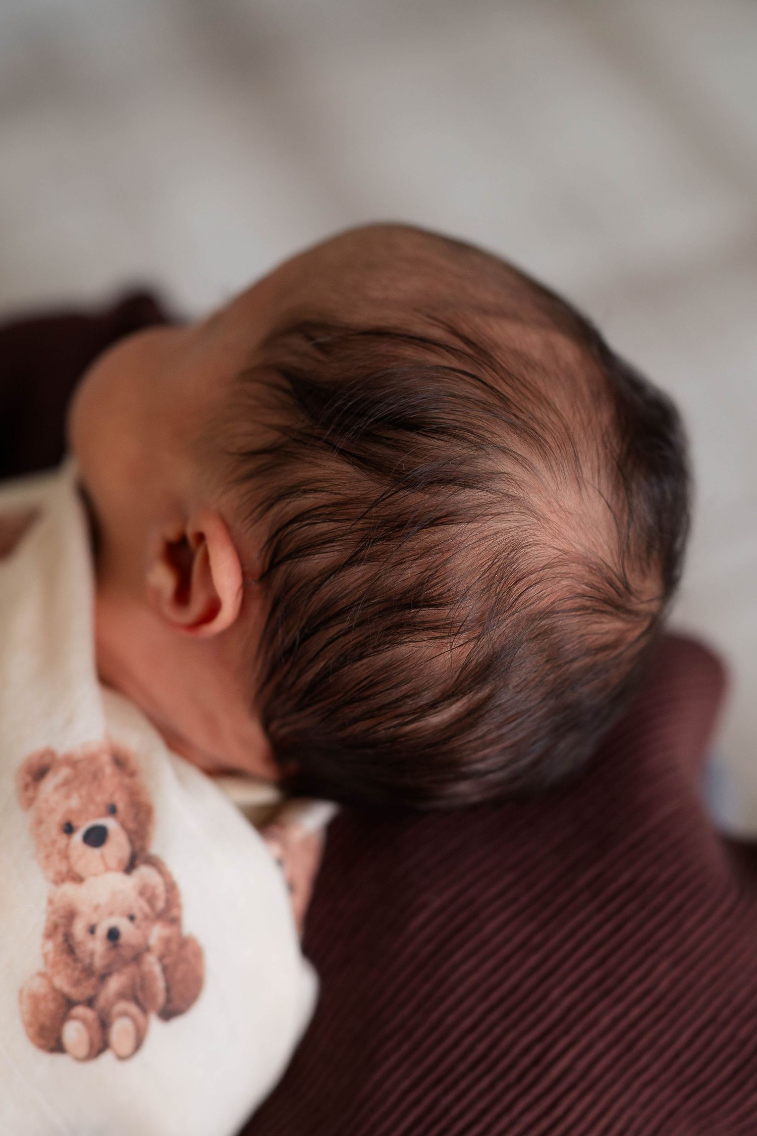 Close-up of a newborn baby's dark hair with a teddy bear patterned blanket nearby.