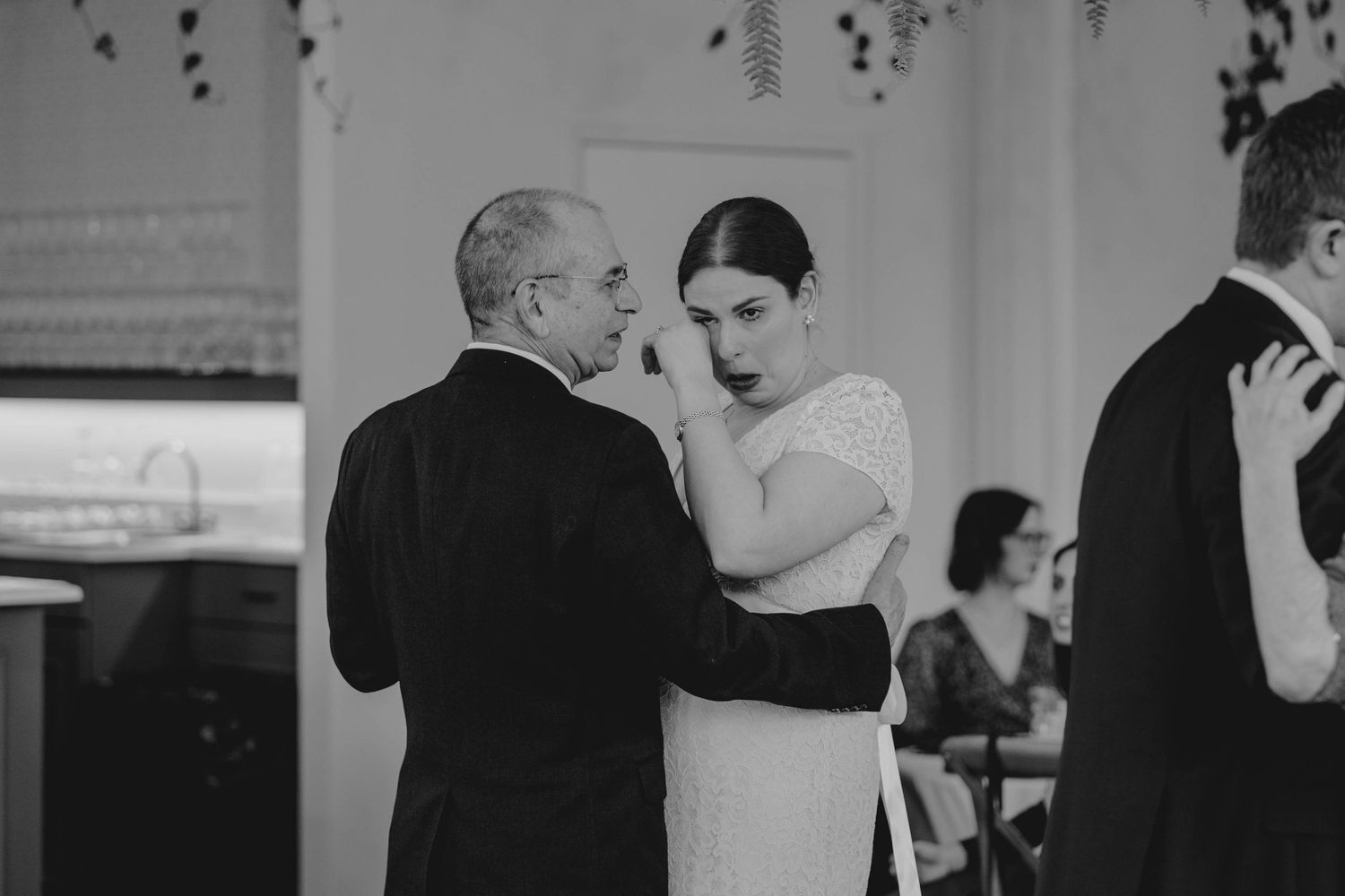 Black and white photo of bride wiping tears during father-daughter wedding dance.