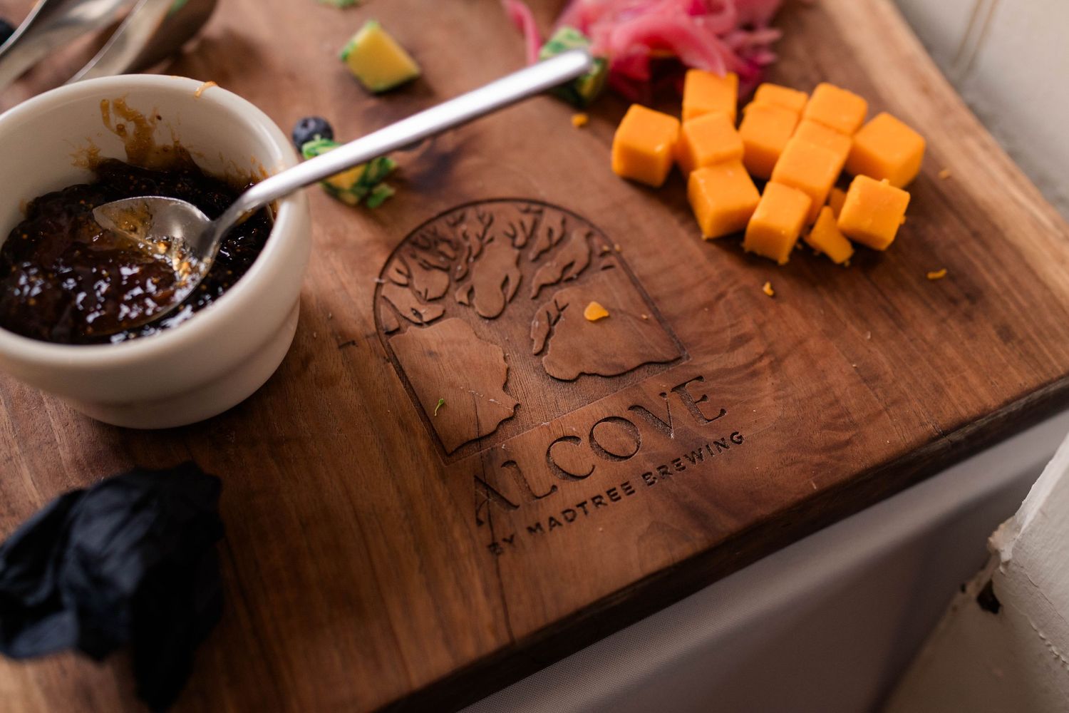 Wooden charcuterie board with cheese, sauce, and Cove at Wayfarer Brewing logo engraving.