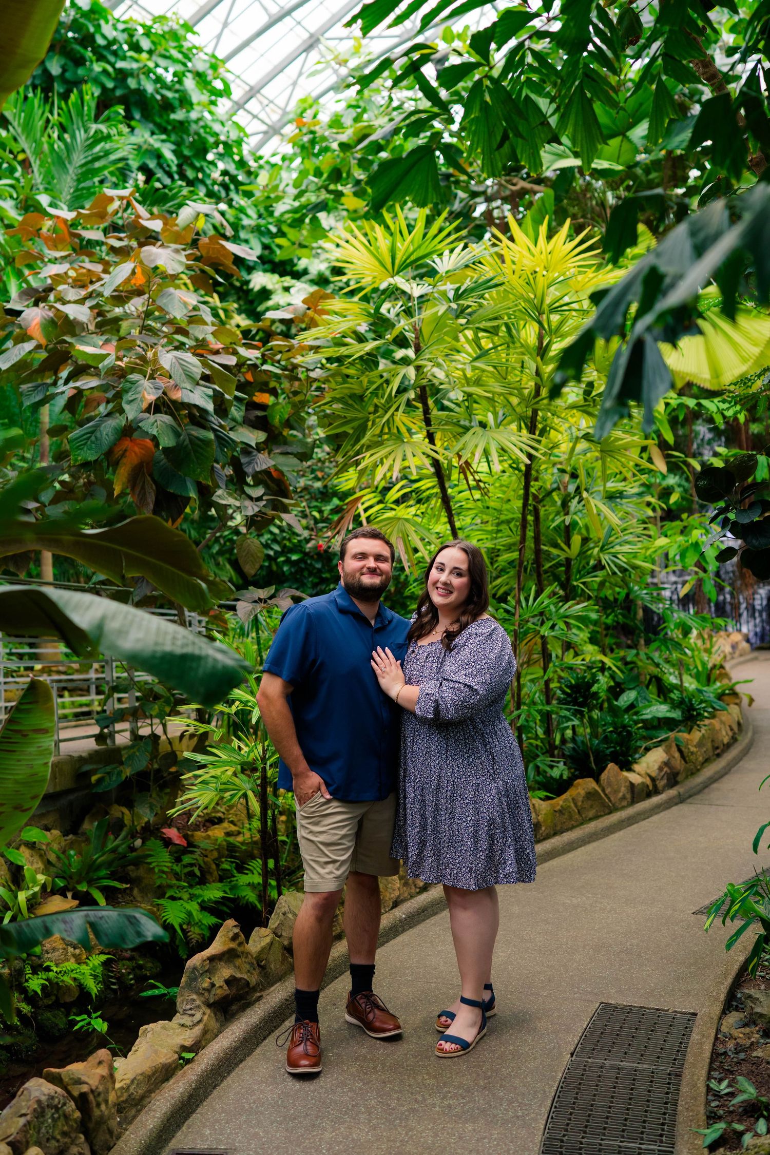Happy couple posing together on a path surrounded by tropical plants in a greenhouse.