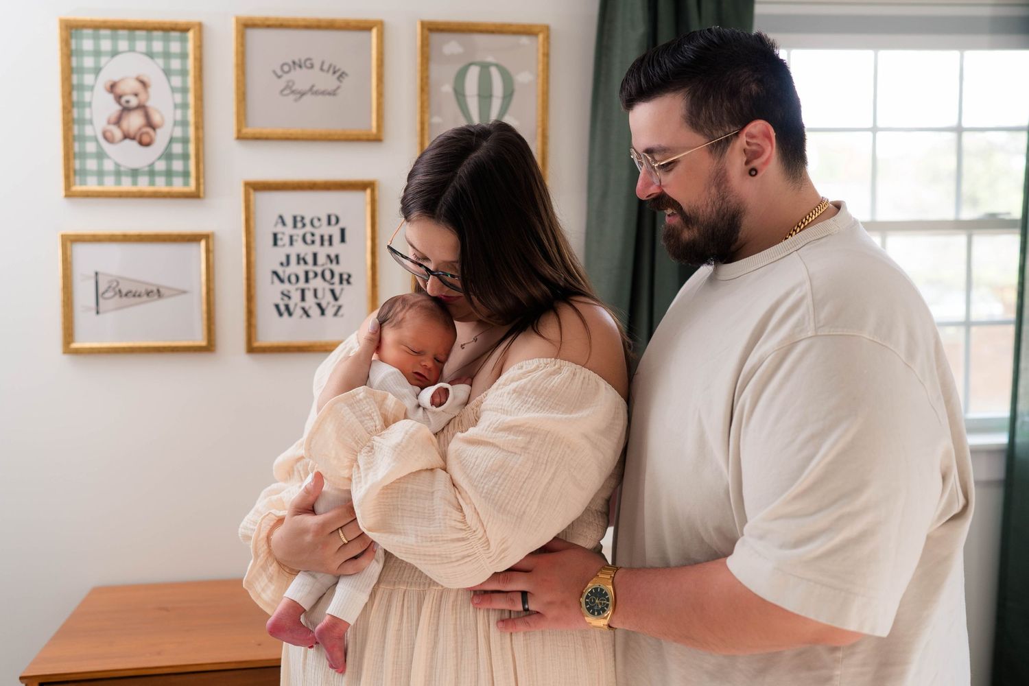 New parents in neutral tones lovingly gaze at their swaddled newborn in a decorated nursery.