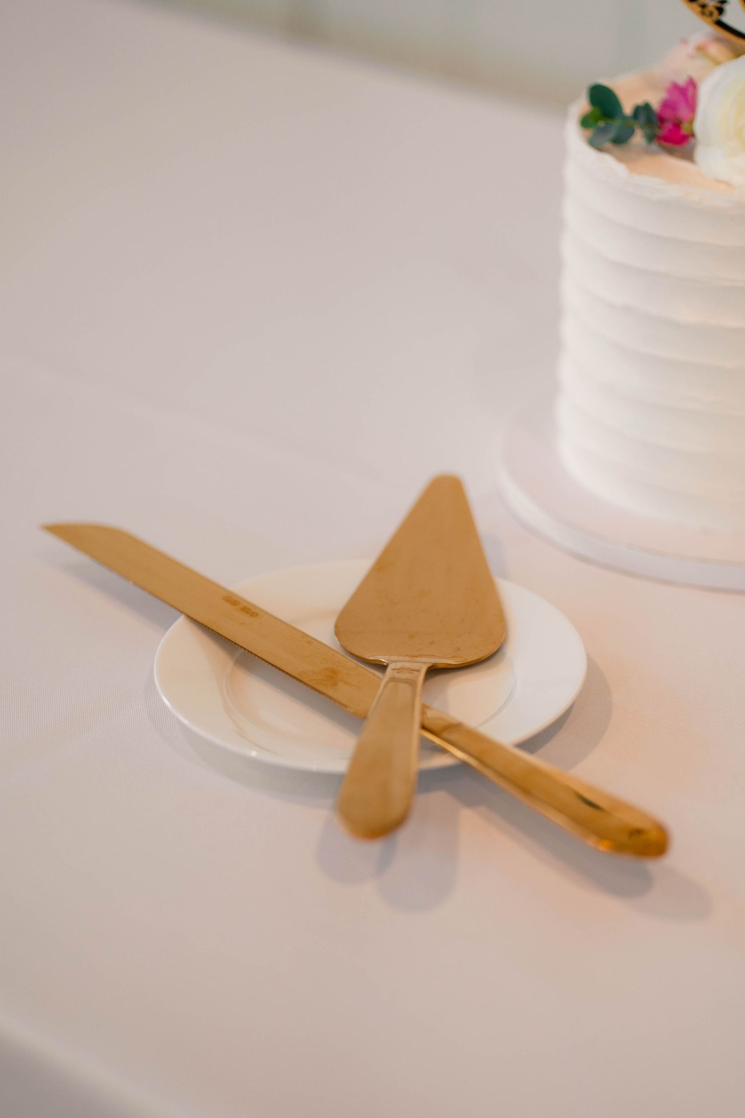 Gold bamboo cake cutting knife and server set crossed on white plate beside wedding cake.