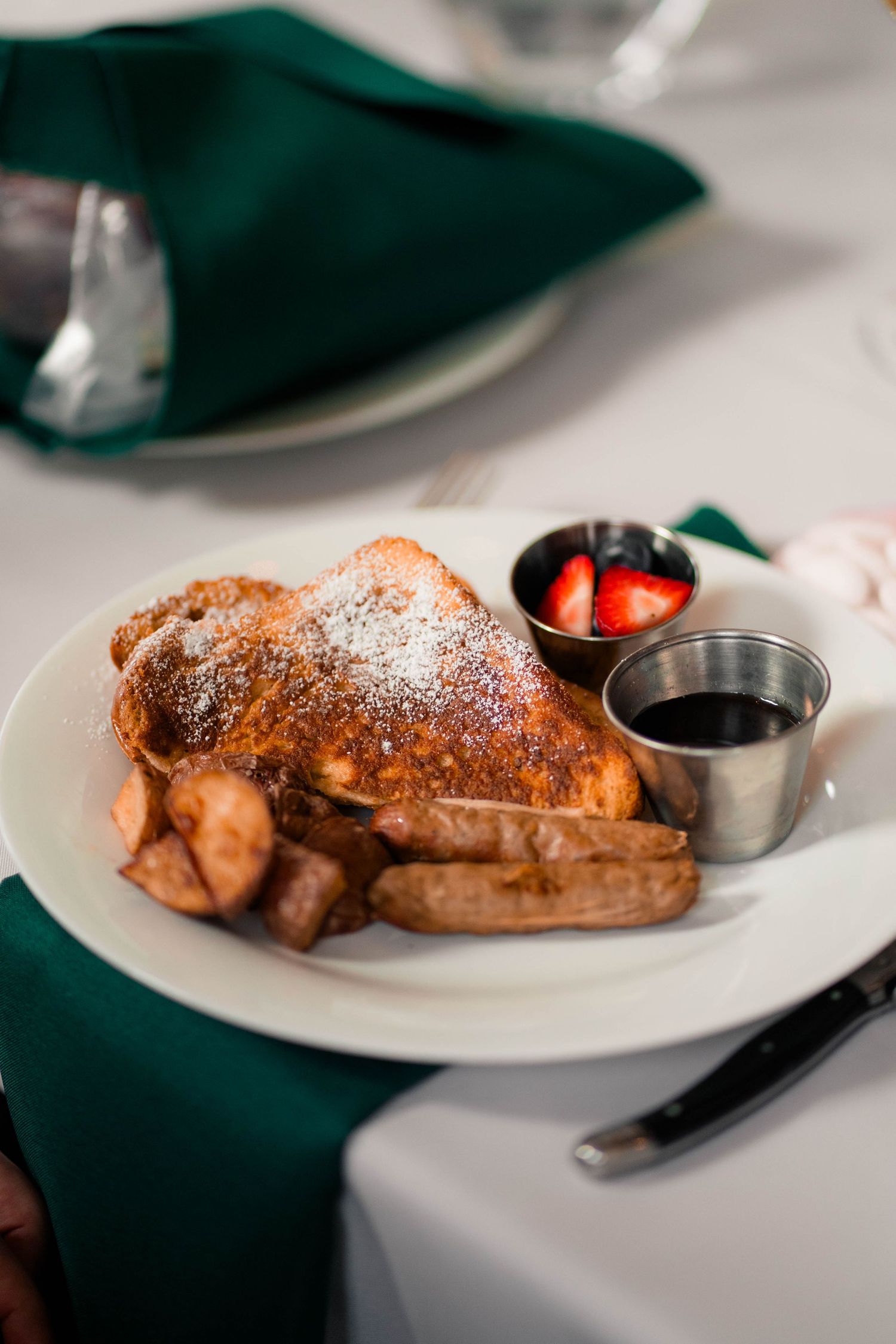 Golden French toast dusted with powdered sugar, served with sausage, fresh berries, and maple syrup.