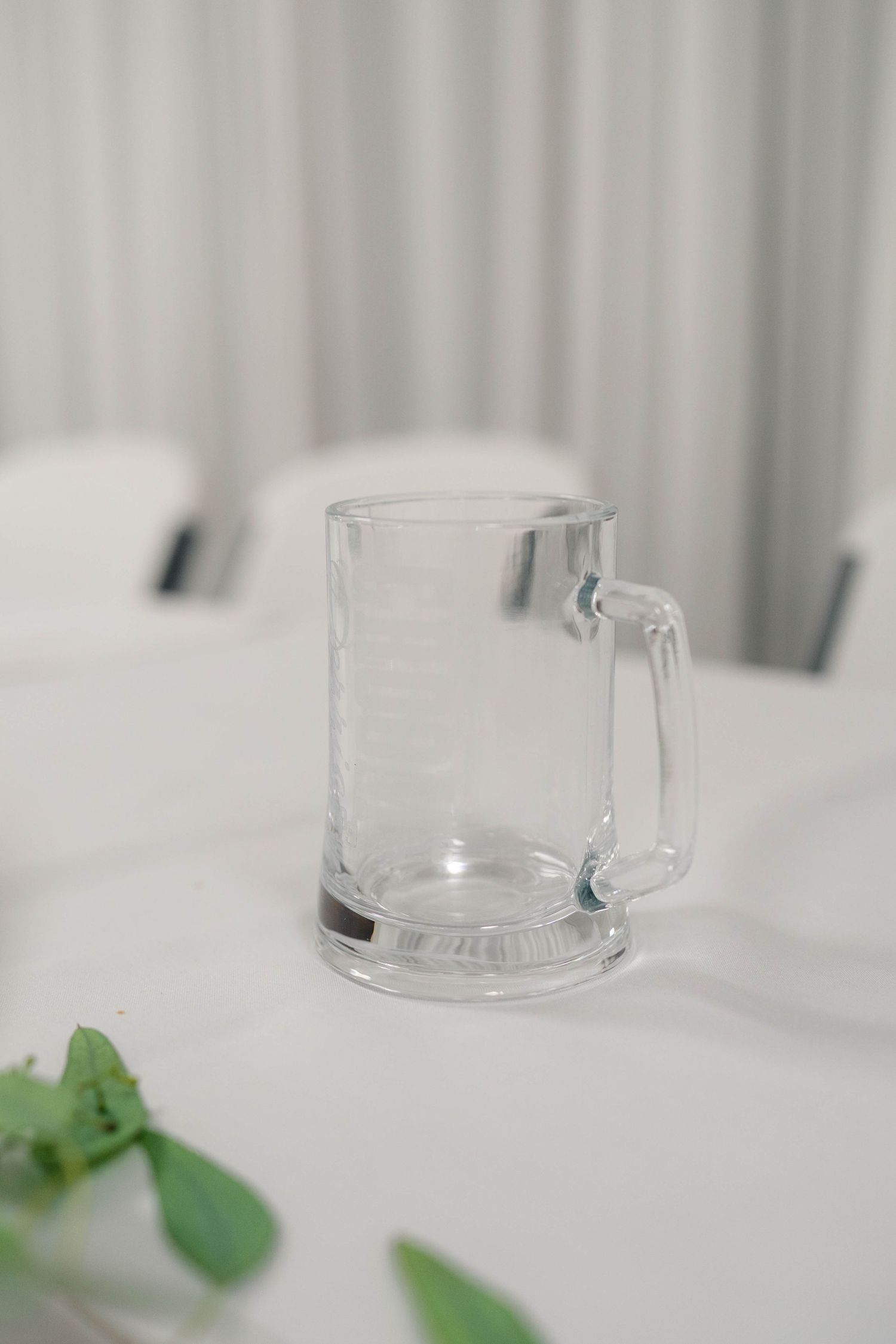 Clear glass beer mug sits on a white linen tablecloth at an elegant wedding reception.