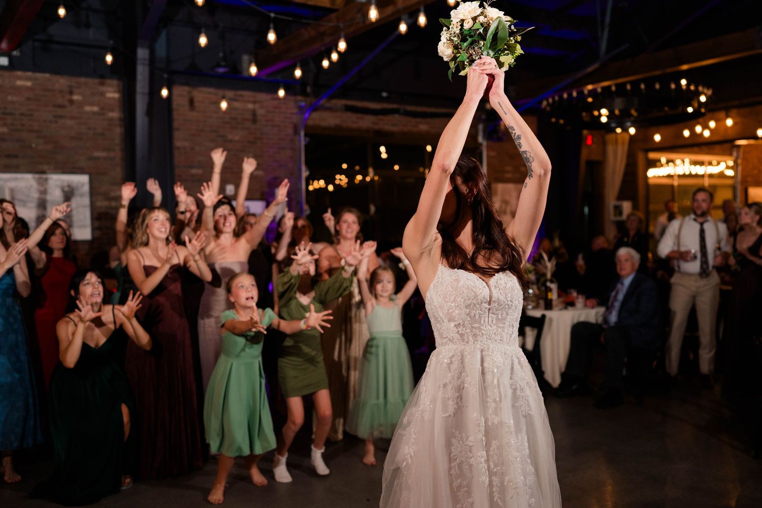 Bride tosses bouquet to excited group of women at indoor wedding reception.