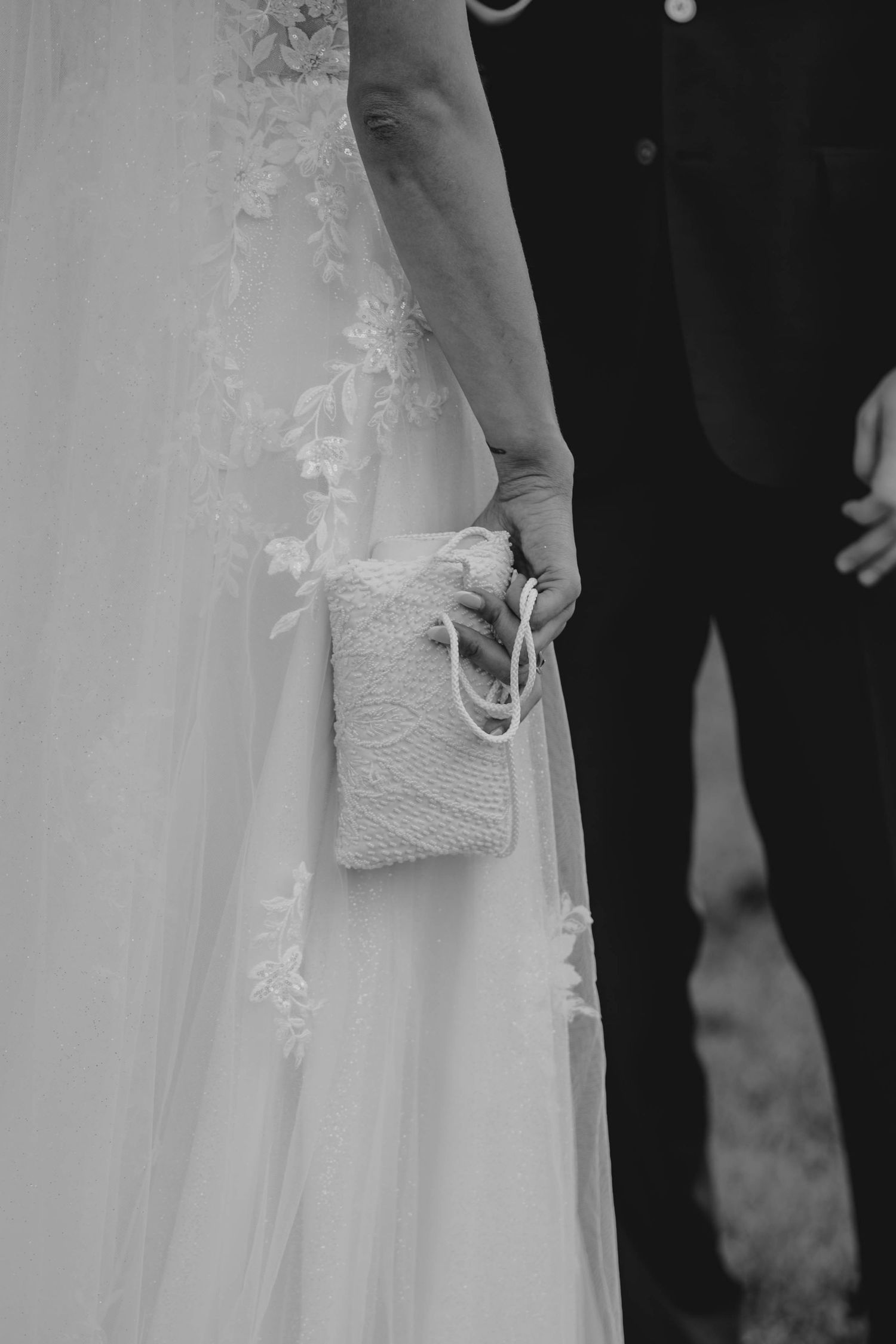 Close-up black and white photo of bride holding small white lace purse in wedding gown.