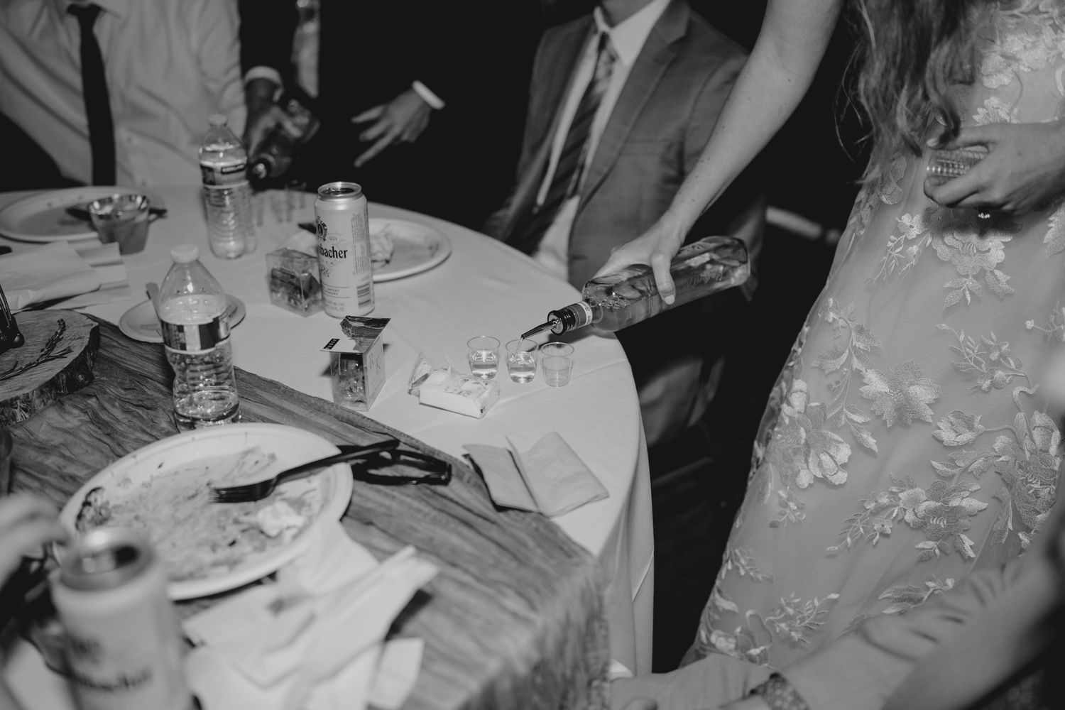 Black and white photo of wedding guests at reception table with drinks and dinnerware.