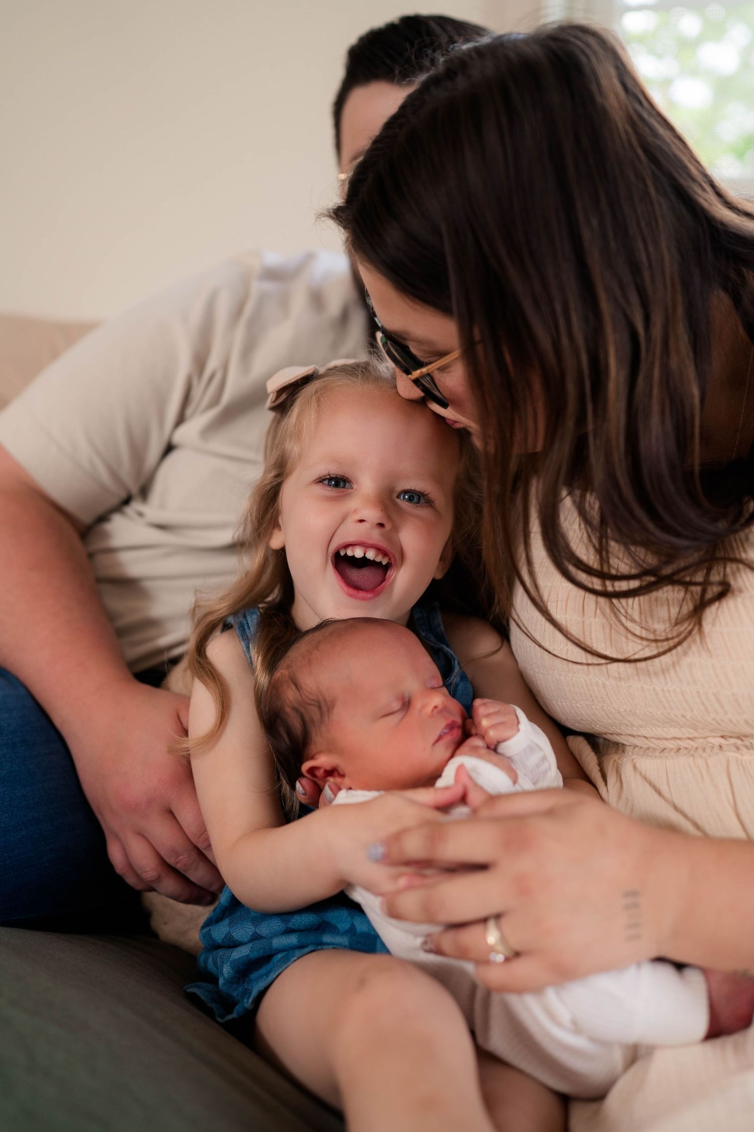 Happy family with newborn baby and excited toddler girl sitting together on couch.