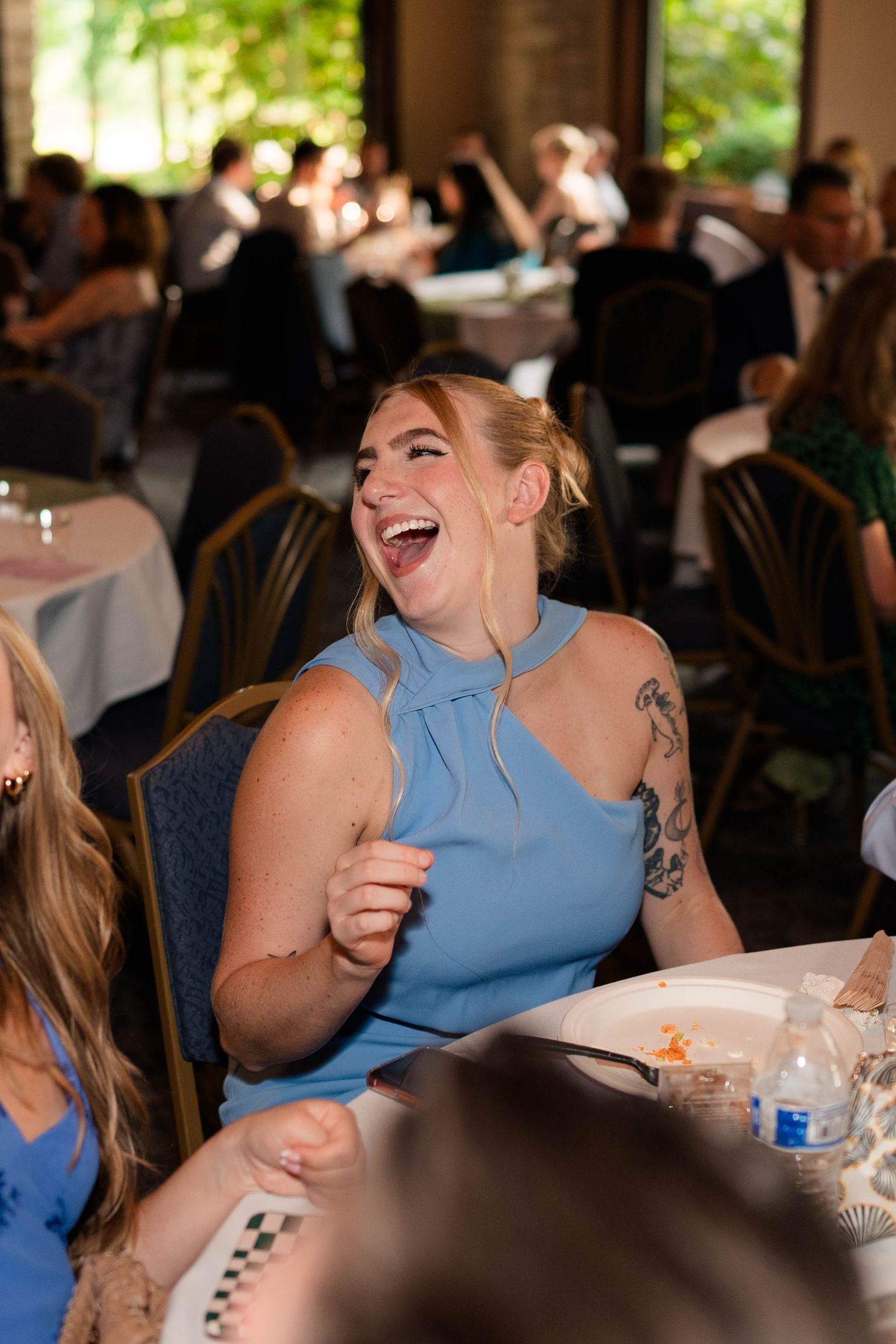 Woman in blue dress laughing joyfully at a wedding reception dinner table.