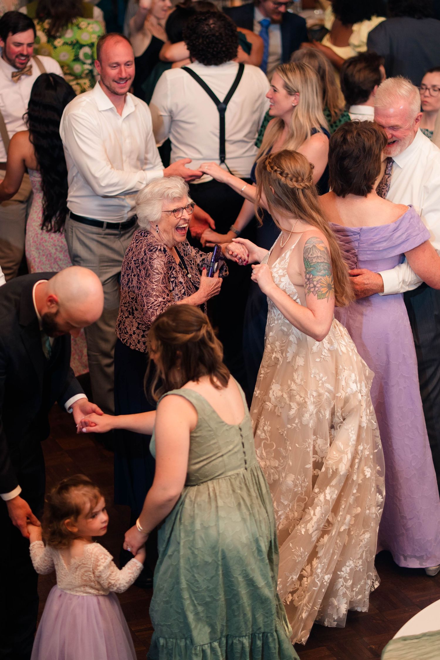 Joyful wedding reception dance floor with bride, family, and guests including elderly woman.