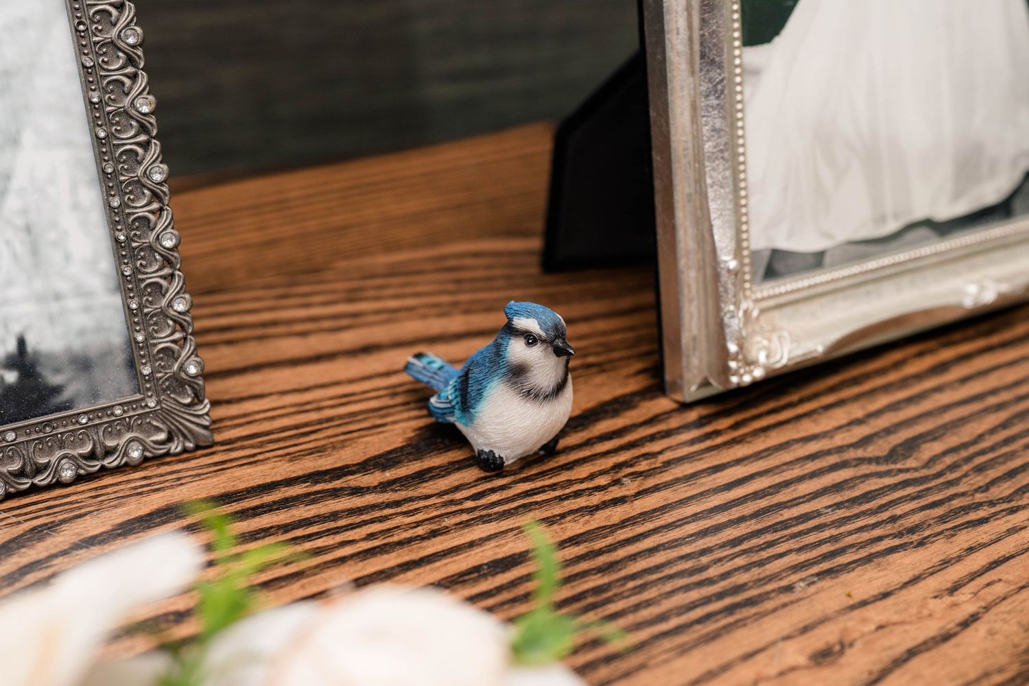 Small decorative blue jay figurine placed between silver picture frames on wooden table.