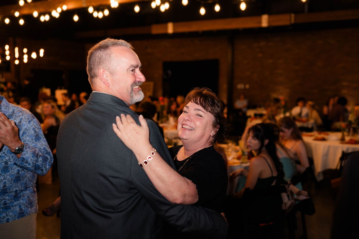 Couple shares a joyful dance together surrounded by guests at a warmly lit wedding reception celebration.