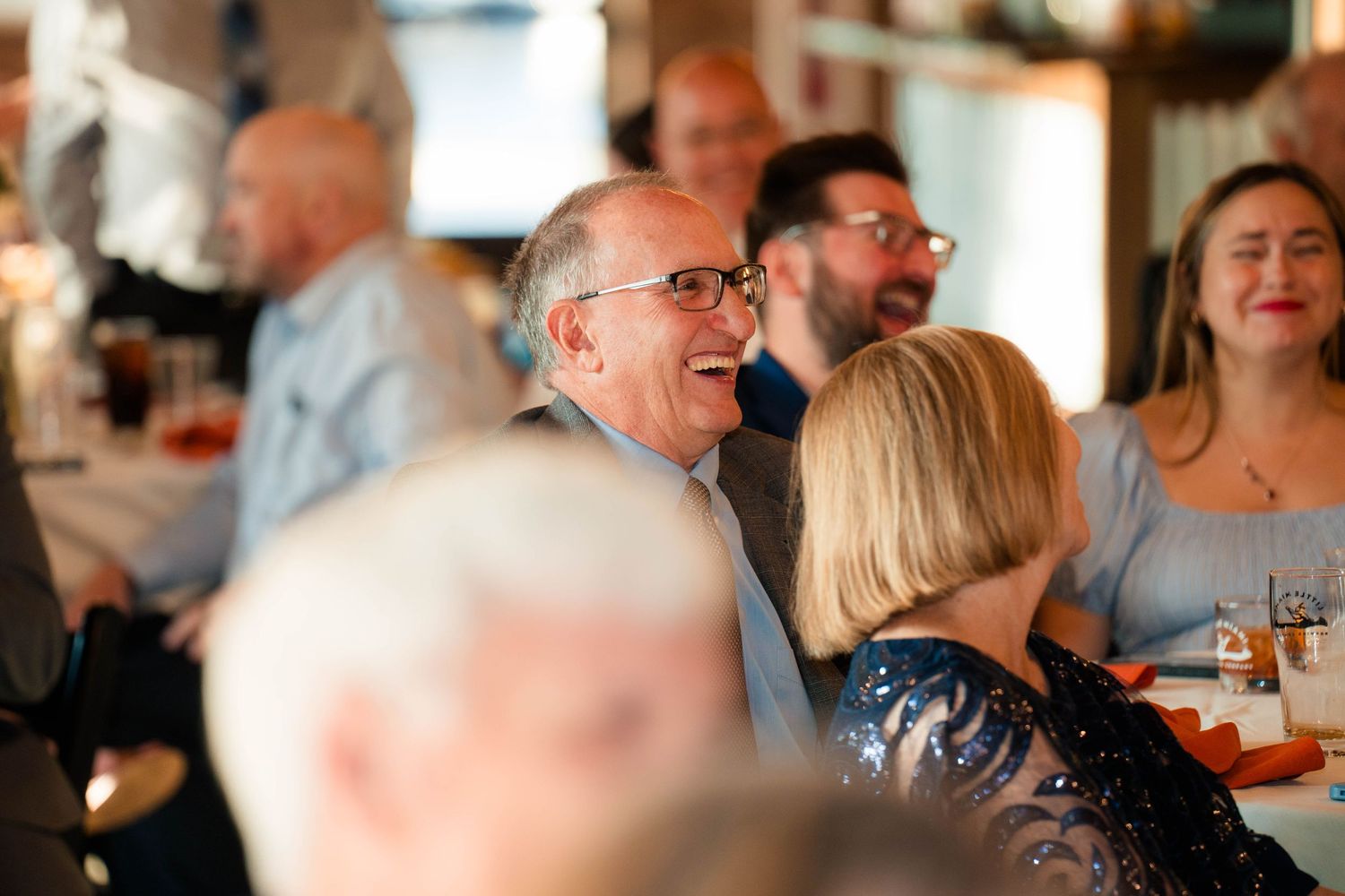 Guests laughing and socializing at a festive indoor dinner celebration or party event.