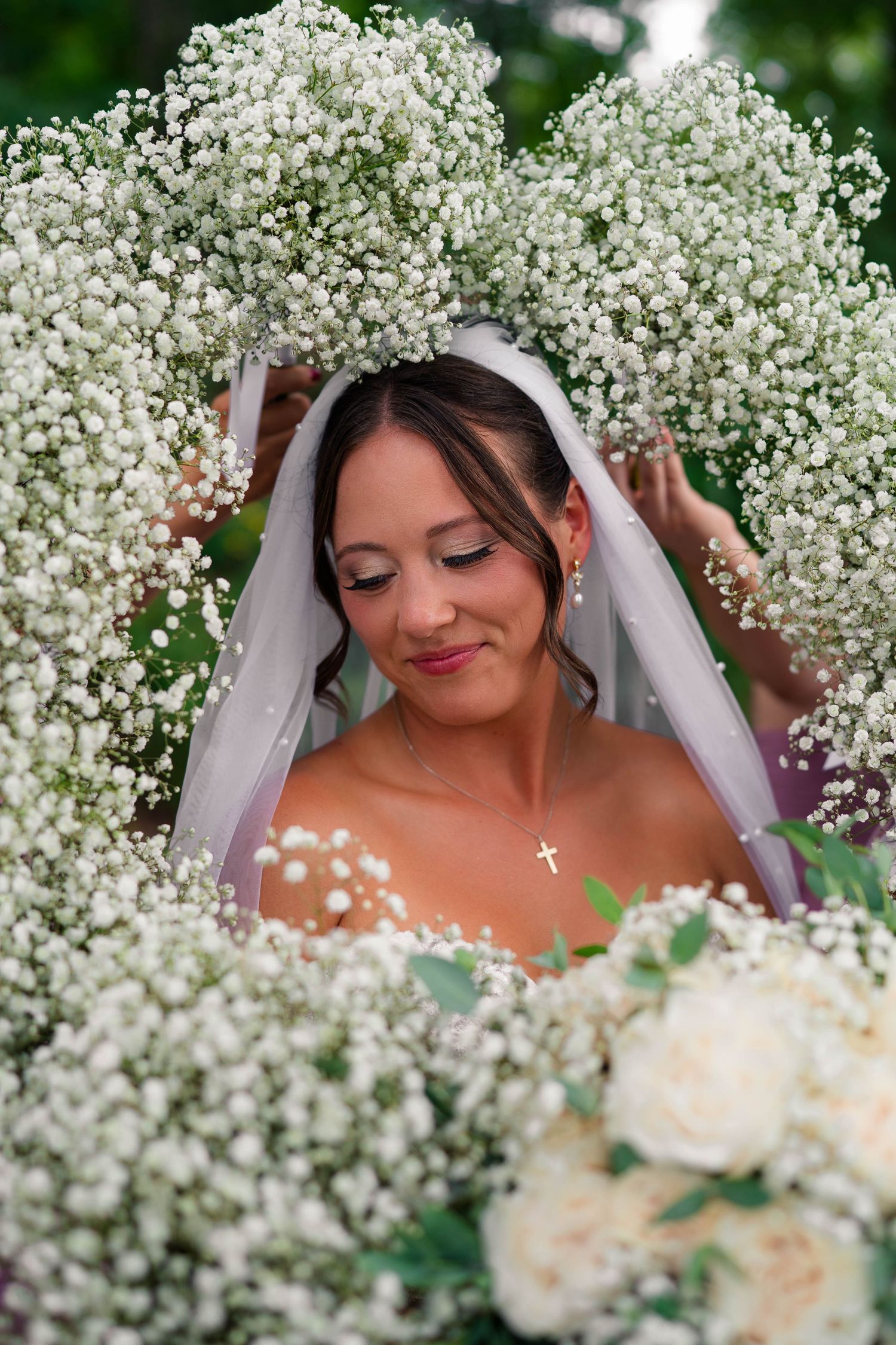 Bride surrounded by baby's breath flowers wearing veil and cross necklace.