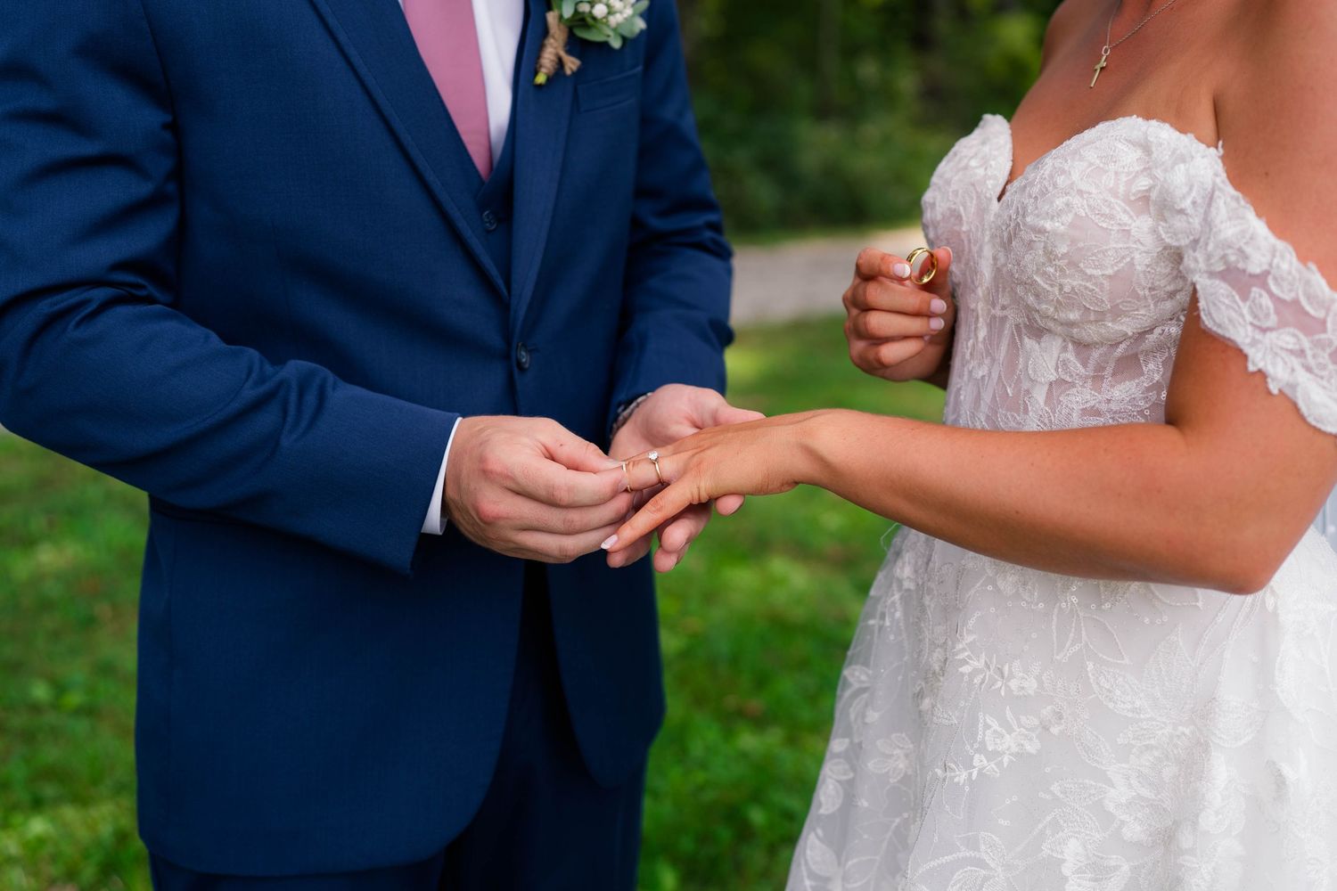 Groom placing wedding ring on bride's finger during outdoor ring exchange ceremony.