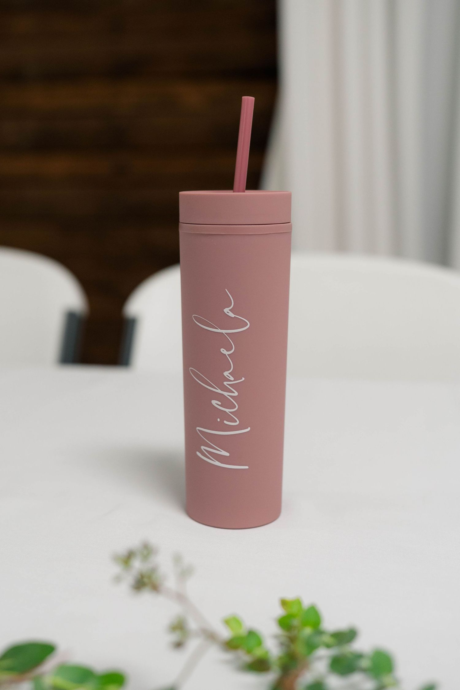 Pink personalized tumbler with name Michaela and straw displayed on white wedding table.