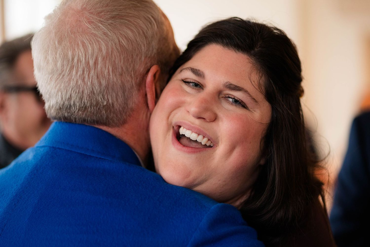 Young woman in blue dress laughs joyfully while embracing a man at a celebratory event.