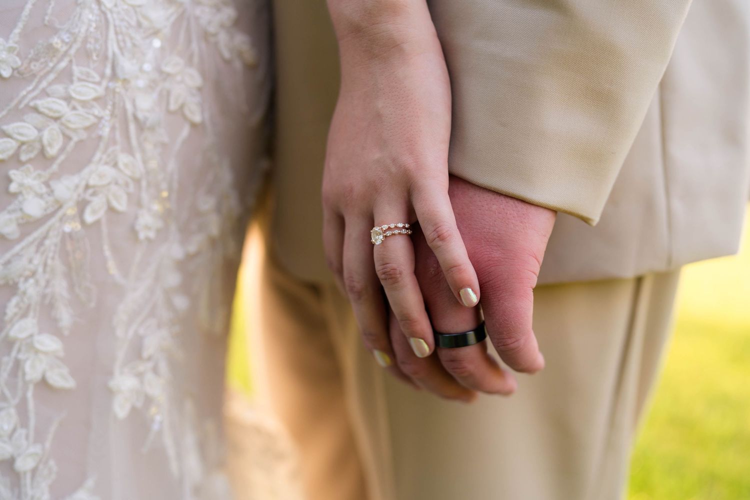 Close-up of bride and groom holding hands, showcasing diamond engagement ring and black wedding band.